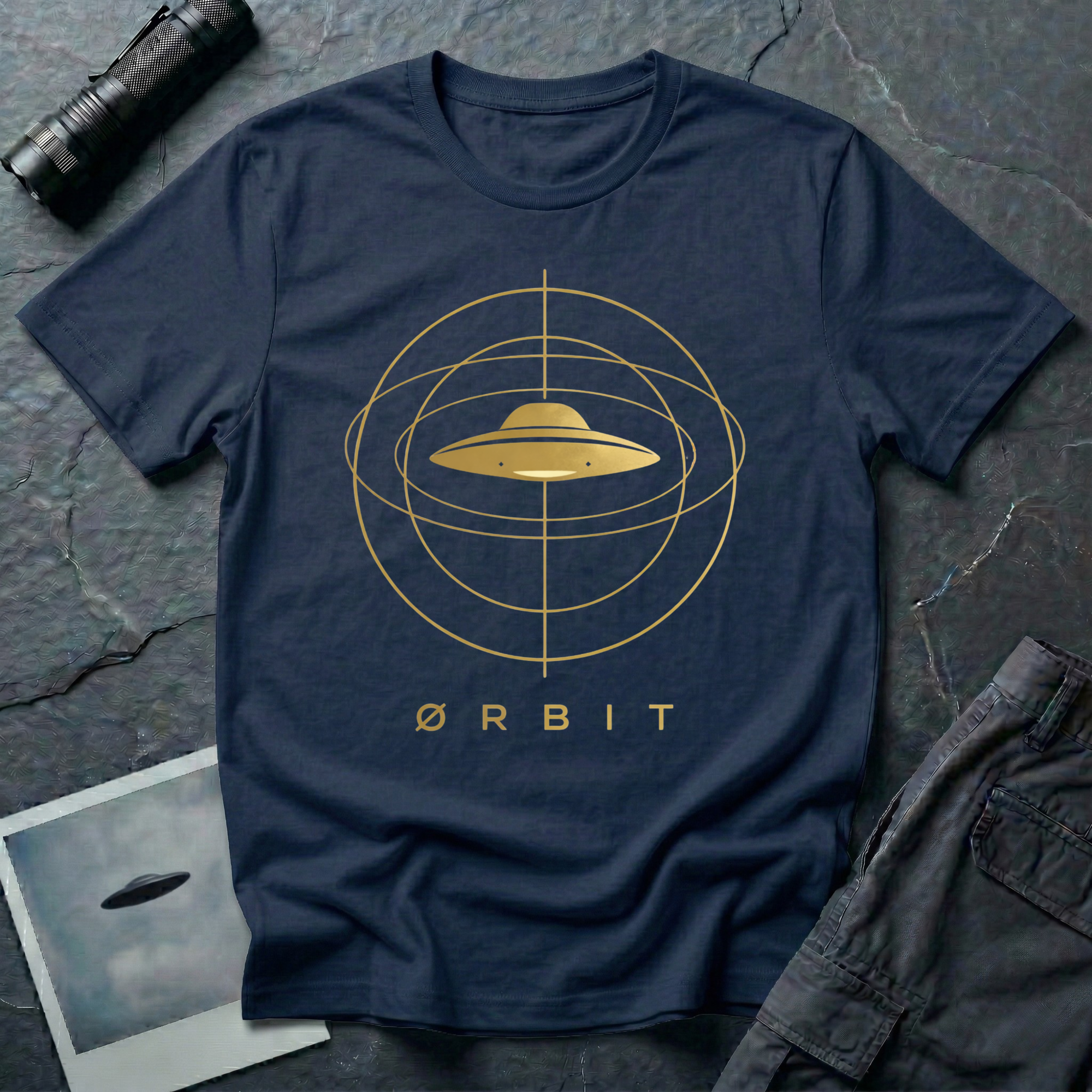 Orbit astronomical UFO t-shirt — flying saucer centred in a gold orbital sphere framework with "Ørbit" sans serif typography on navy cotton tee