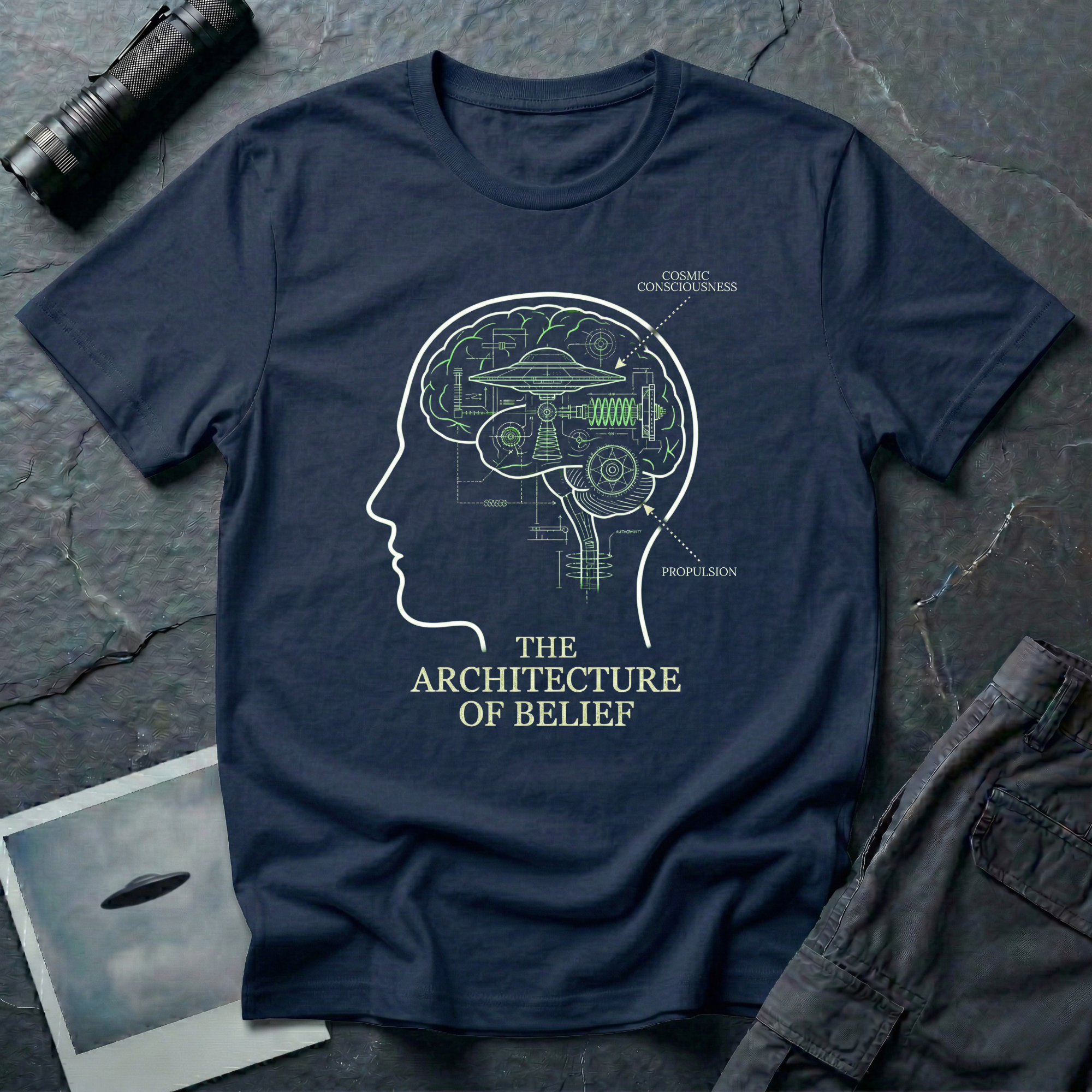 The Architecture of Belief consciousness UFO t-shirt — profile head with cutaway brain containing flying saucer and mechanical components in white and green on navy cotton tee
