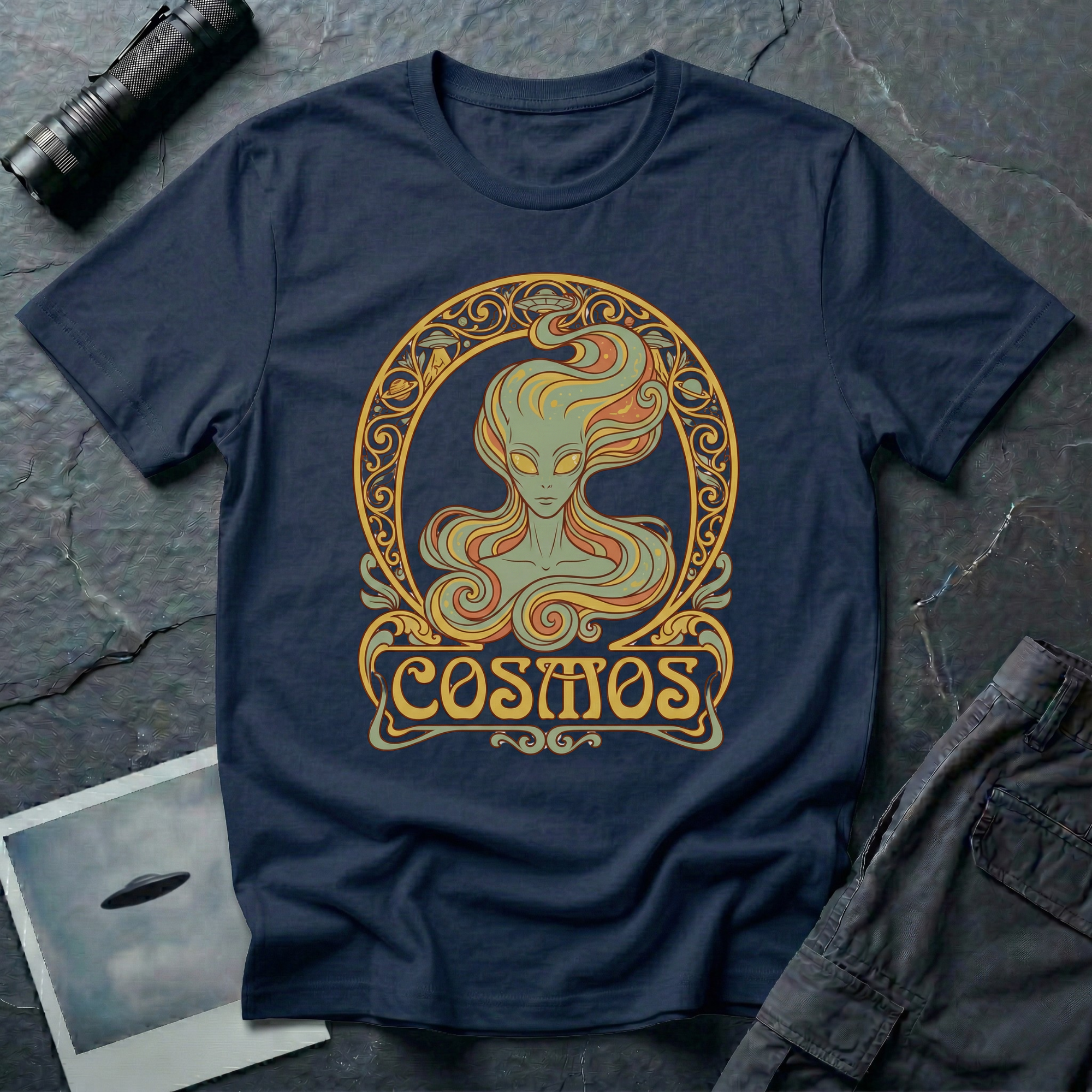 Cosmos Art Nouveau alien t-shirt — green grey alien portrait with large almond eyes and flowing orange hair in ornate gold decorative frame with scrollwork and "Cosmos" banner on navy cotton tee