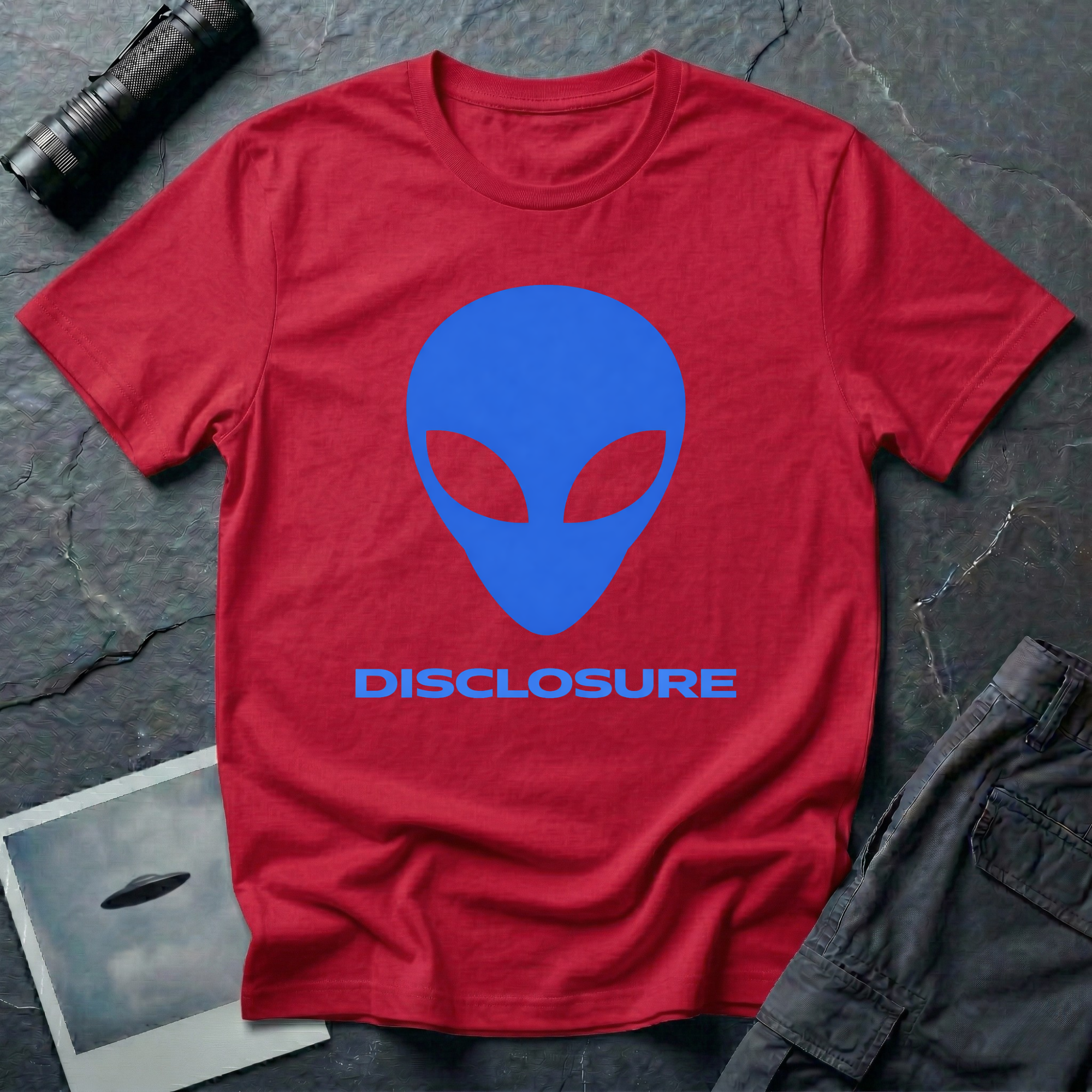 Alien Disclosure grey alien t-shirt — classic bulbous-head alien with almond eyes in electric blue on red unisex cotton tee
