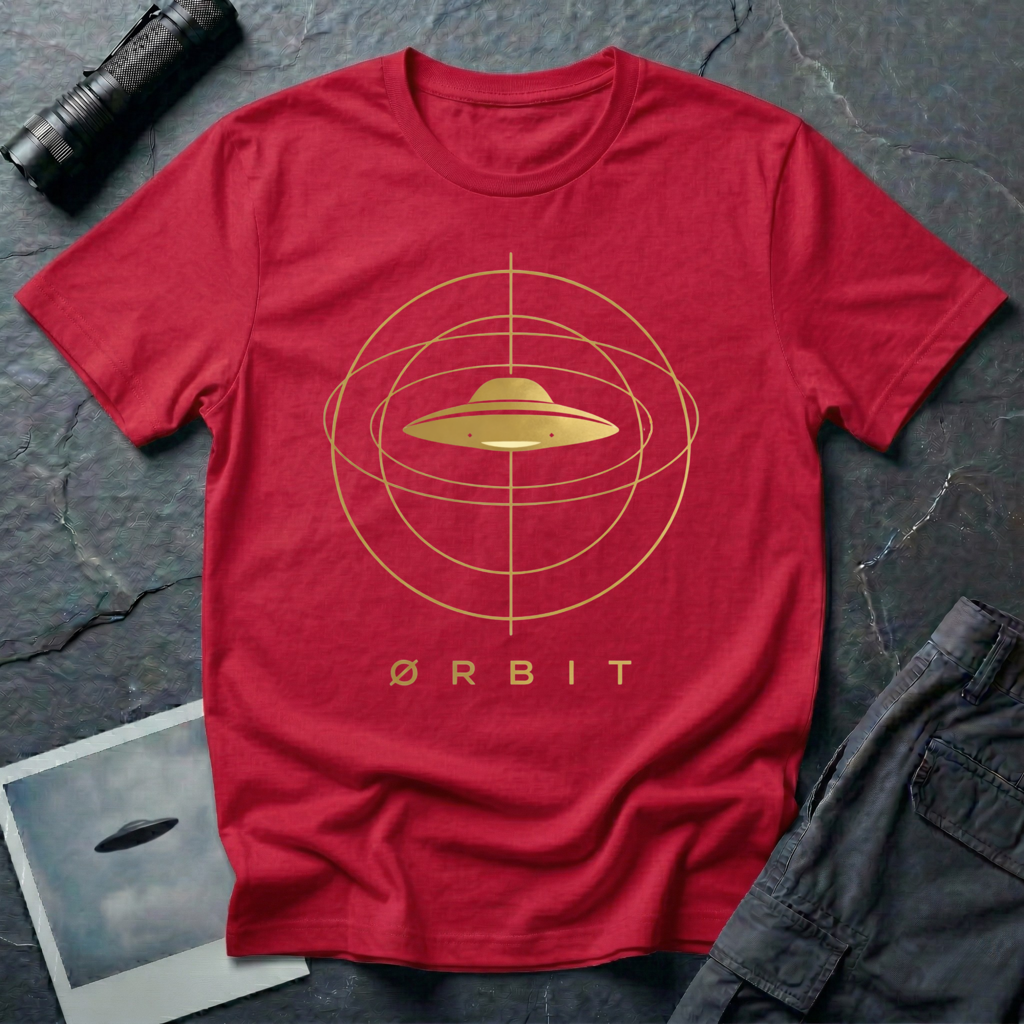 Orbit astronomical UFO t-shirt — flying saucer centred in a gold orbital sphere framework with "Ørbit" sans serif typography on red cotton tee