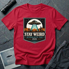 Stay Weird desert UFO t-shirt — tour-poster badge with flying saucer over desert landscape and cacti on red cotton tee