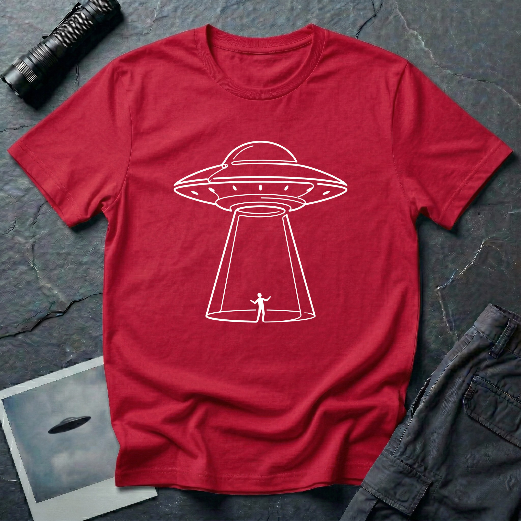 One Line UFO minimalist line art t-shirt — hand-drawn flying saucer beaming down over a tiny stick figure in one continuous white line on red cotton tee
