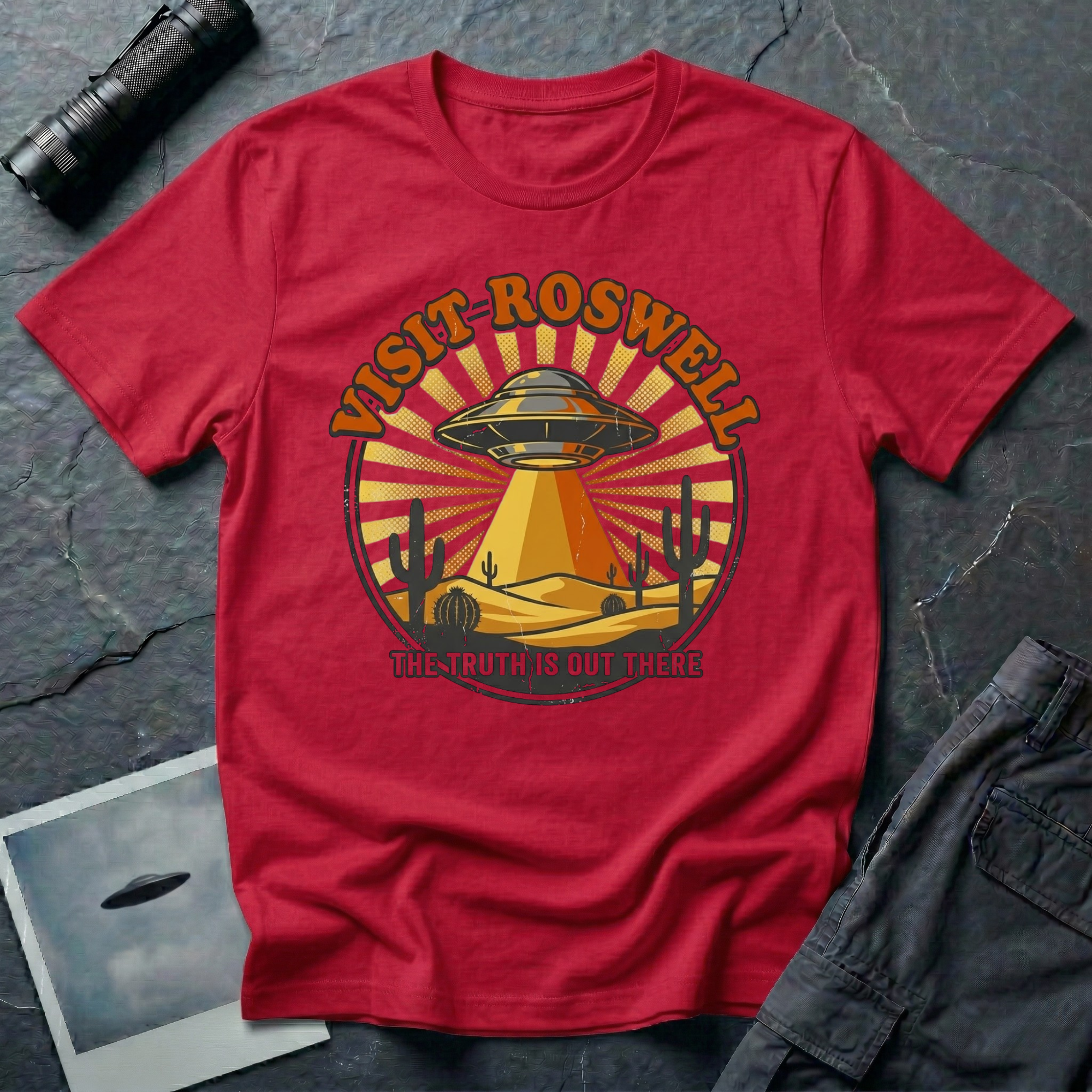 Visit Roswell UFO t-shirt — vintage circular tourism badge with flying saucer beaming over desert cacti in rust and mustard tones on redcotton tee