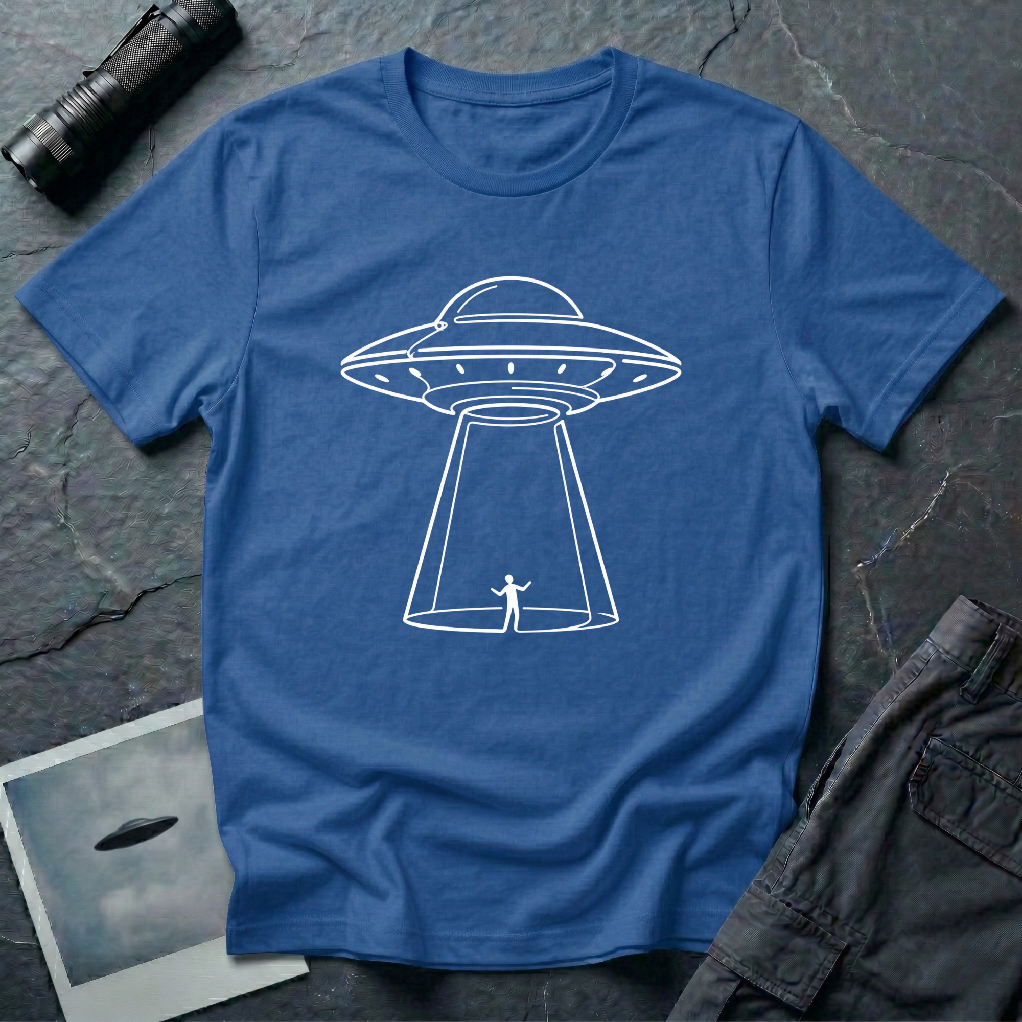 One Line UFO minimalist line art t-shirt — hand-drawn flying saucer beaming down over a tiny stick figure in one continuous white line on blue cotton tee