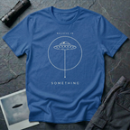 Believe in Something minimalist UFO t-shirt — flying saucer inside a circle with a suspended plumb line in cream on blue cotton tee