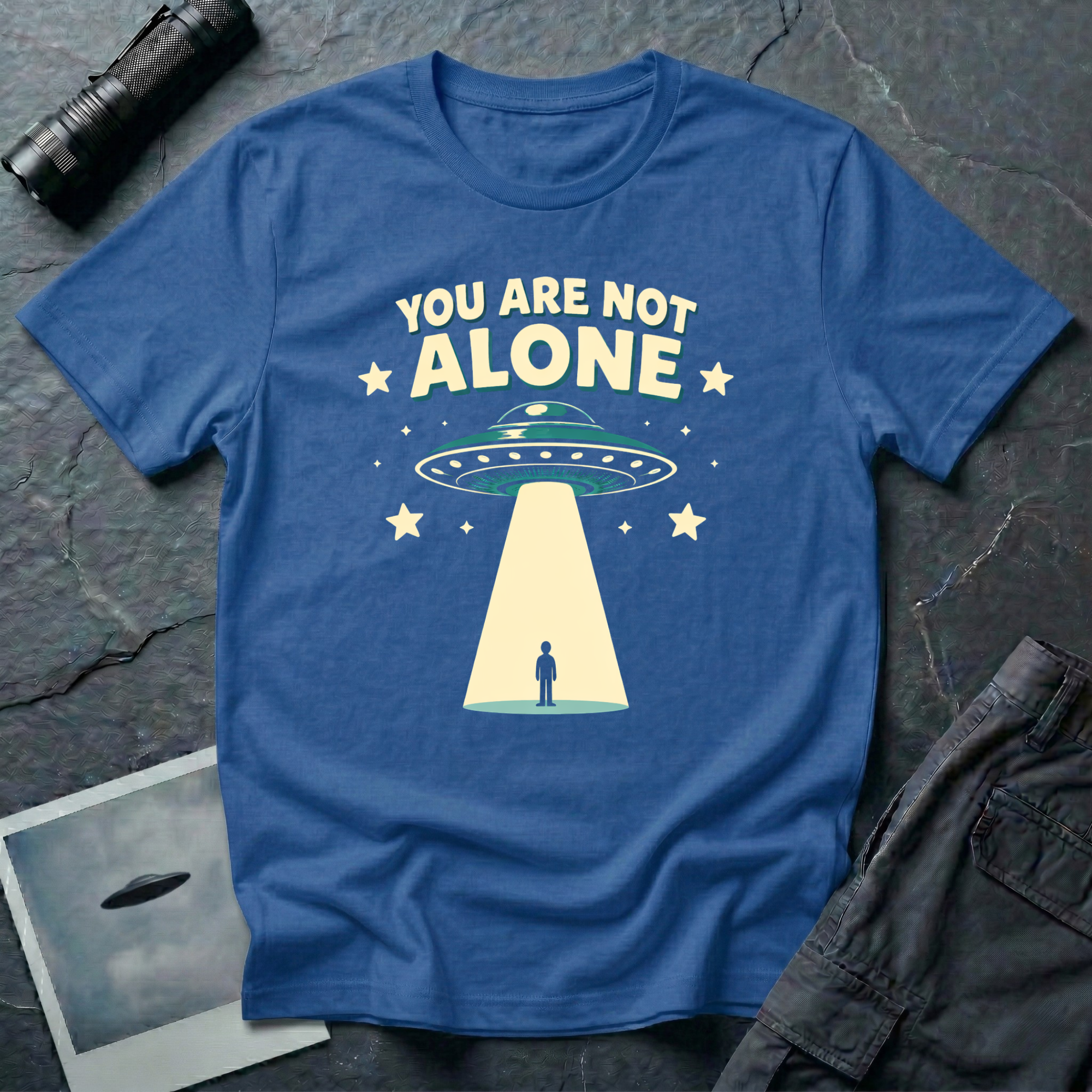 You Are Not Alone friendly UFO t-shirt — retro saucer beaming down on a calm human figure with "You Are Not Alone" text on blue cotton tee