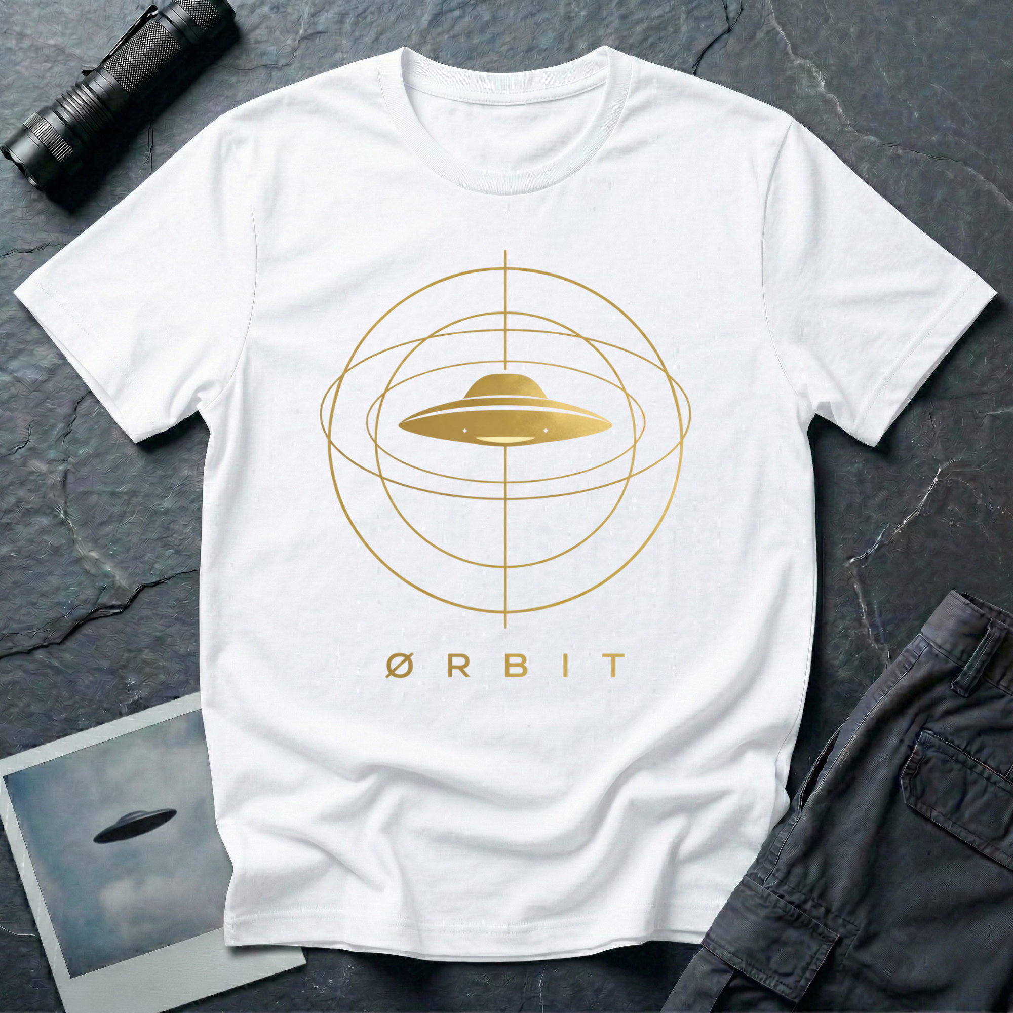 Orbit astronomical UFO t-shirt — flying saucer centred in a gold orbital sphere framework with "Ørbit" sans serif typography on white cotton tee
