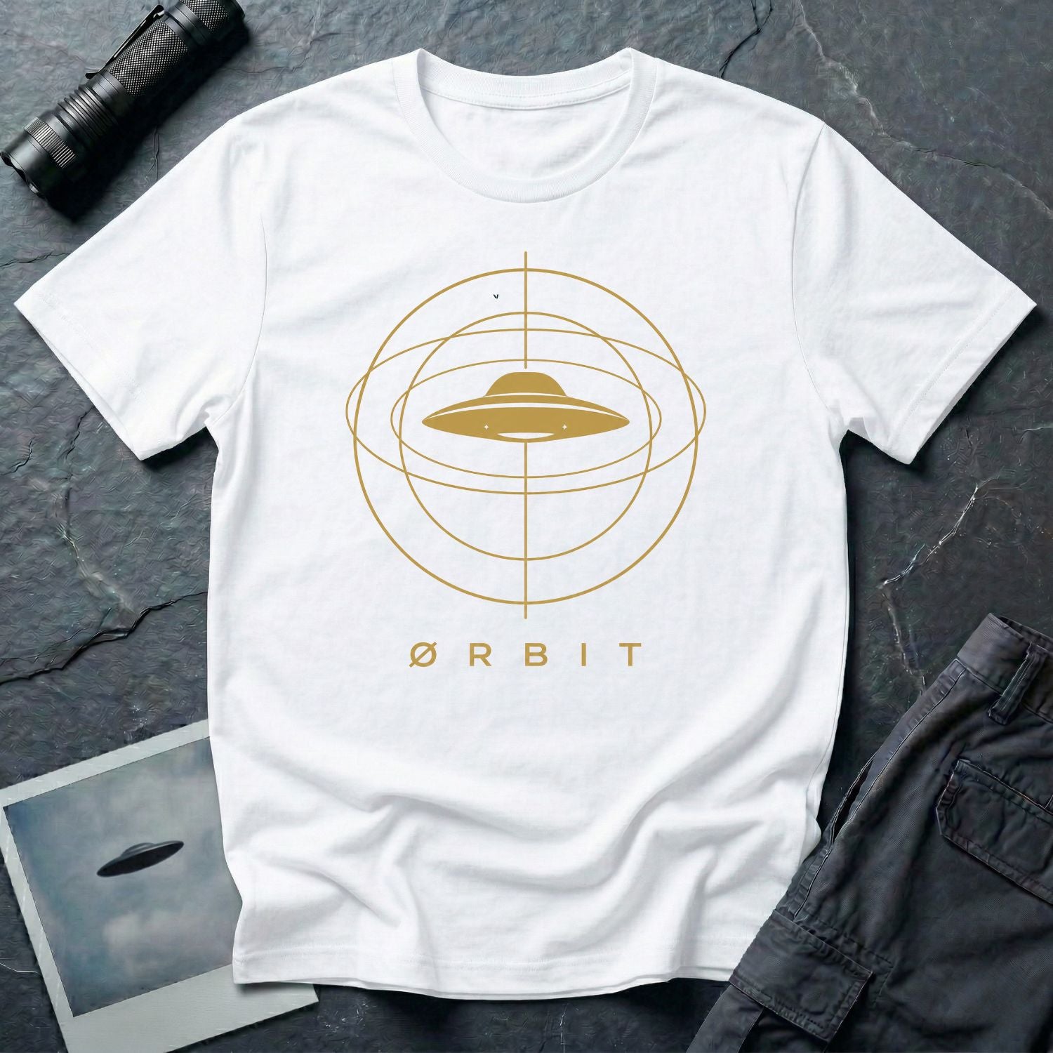 Orbit astronomical UFO t-shirt — flying saucer centred in a gold orbital sphere framework with "Ørbit" sans serif typography on white cotton tee