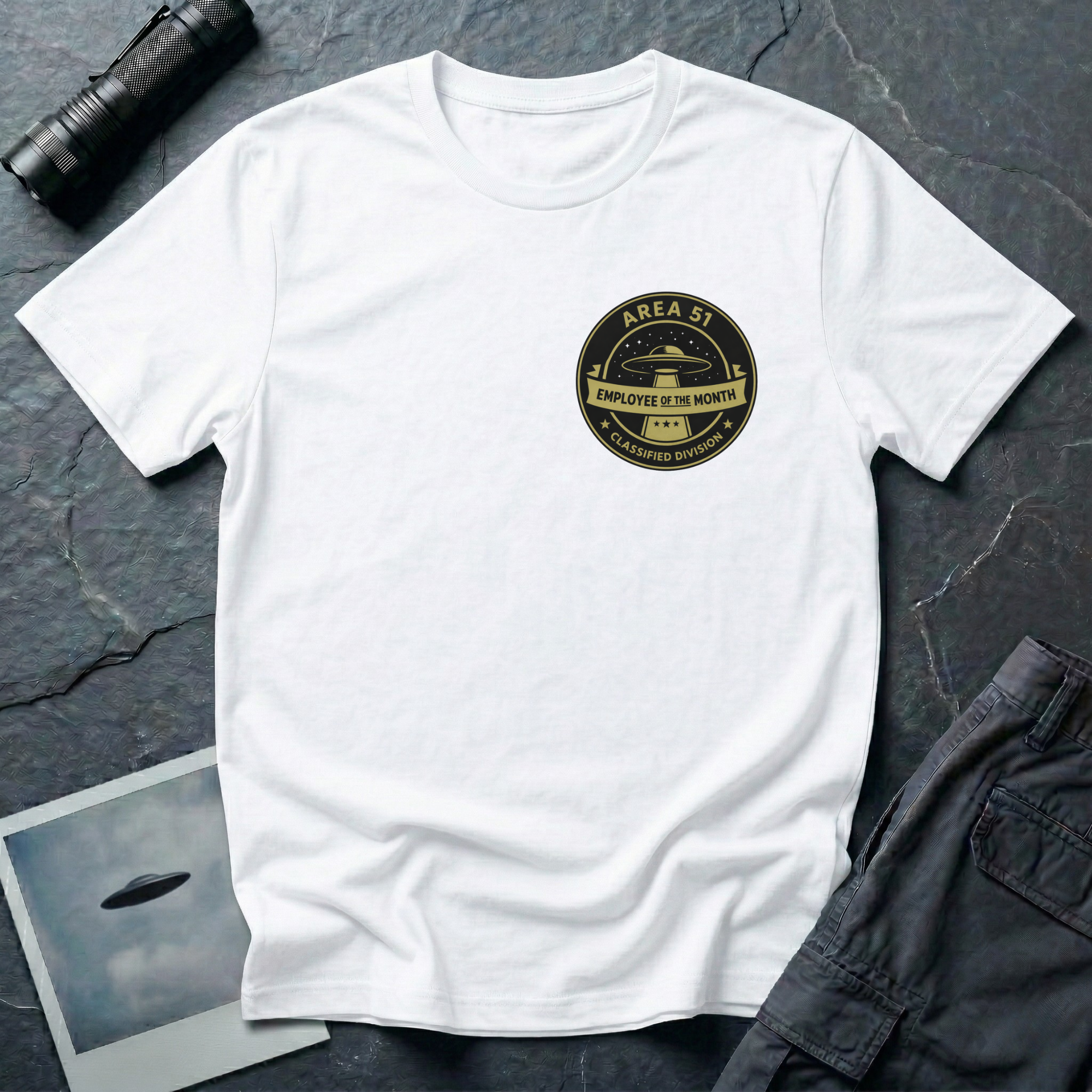 Area 51 Employee Of The Month UFO t-shirt — vintage circular badge with classic flying saucer, "Area 51" and "Classified Division" arc text, "Employee of the Month" ribbon banner in olive and black on upper-left chest of white cotton tee