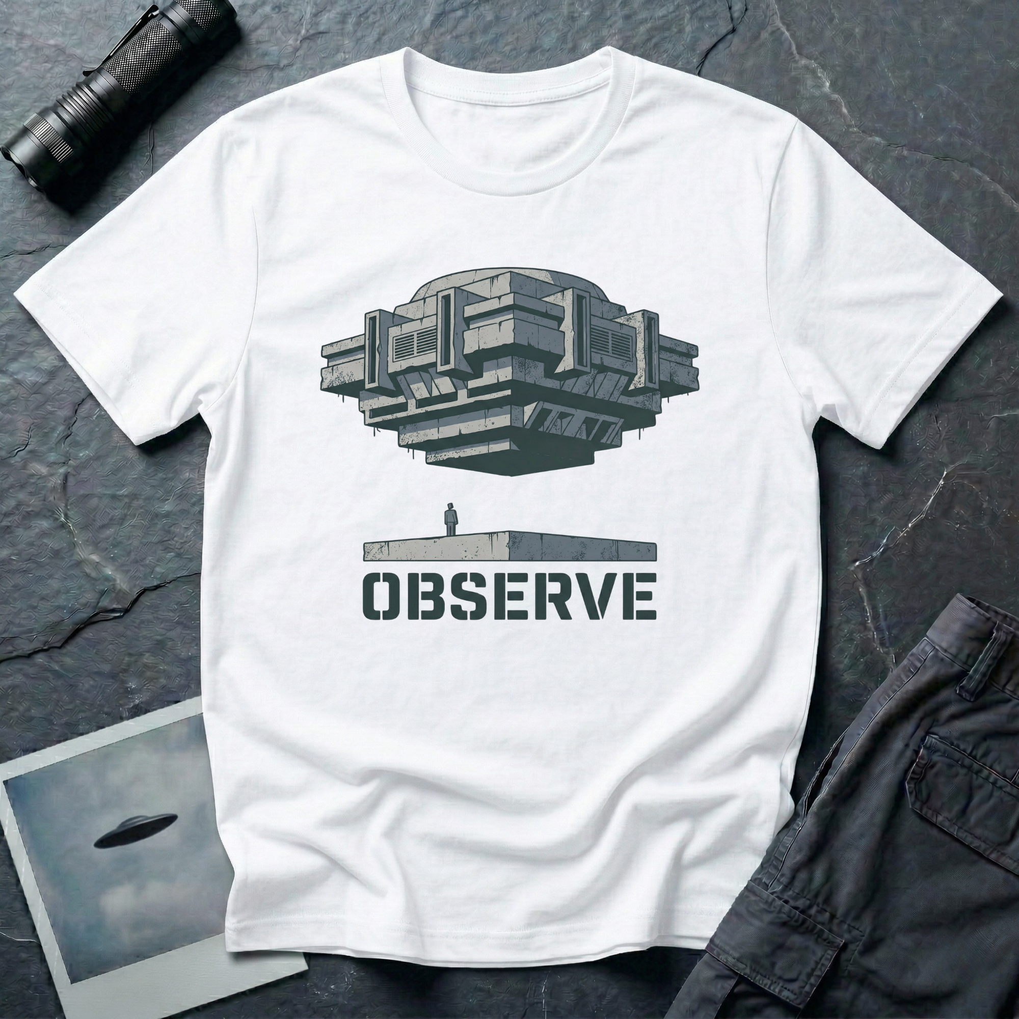 Observe Brutalist UFO t-shirt — massive concrete architectural craft hovering over small figure on plinth with "Observe" stencil type on white cotton tee