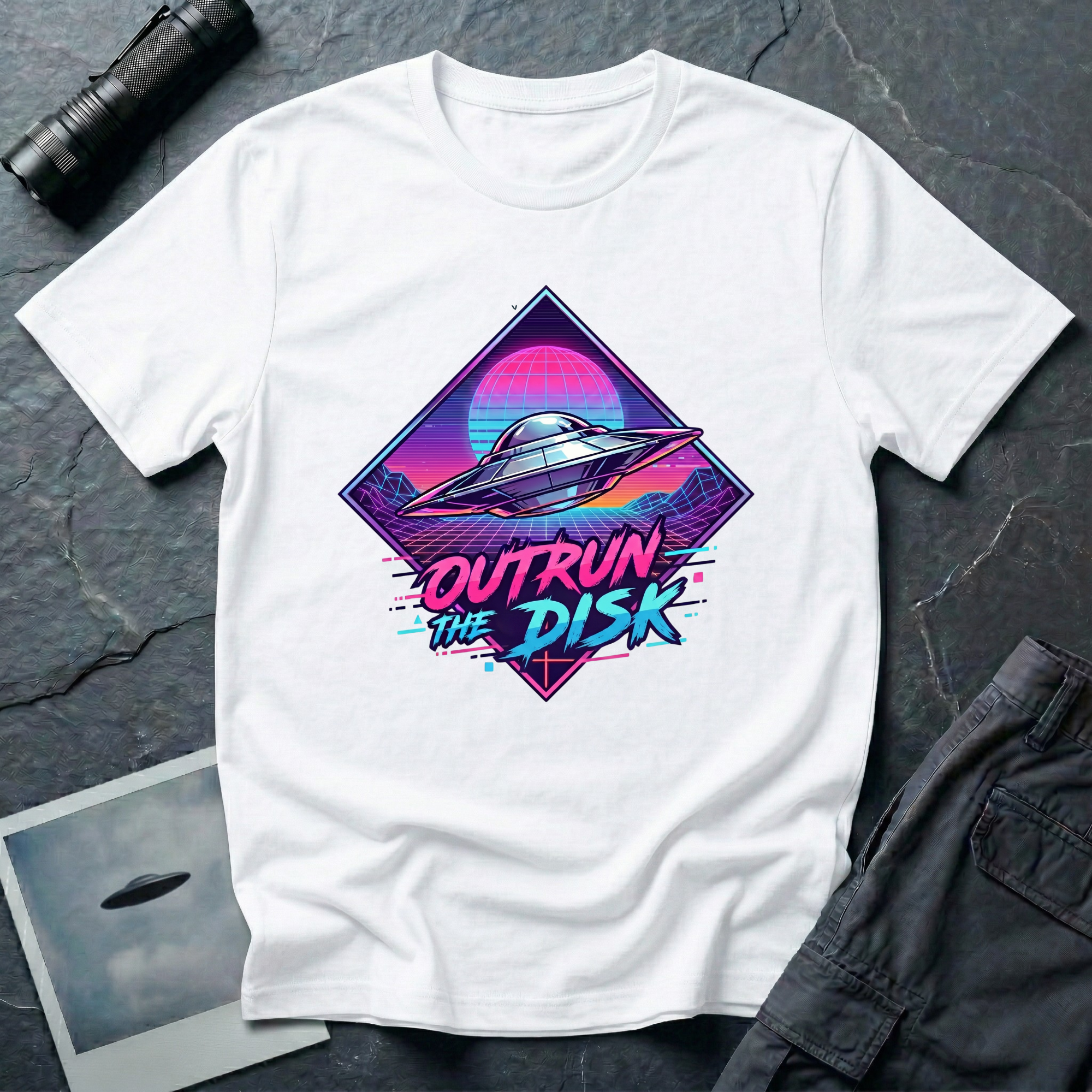 Outrun The Disk synthwave UFO t-shirt — chrome saucer across neon grid landscape with wireframe sun and retrowave typography on white cotton tee