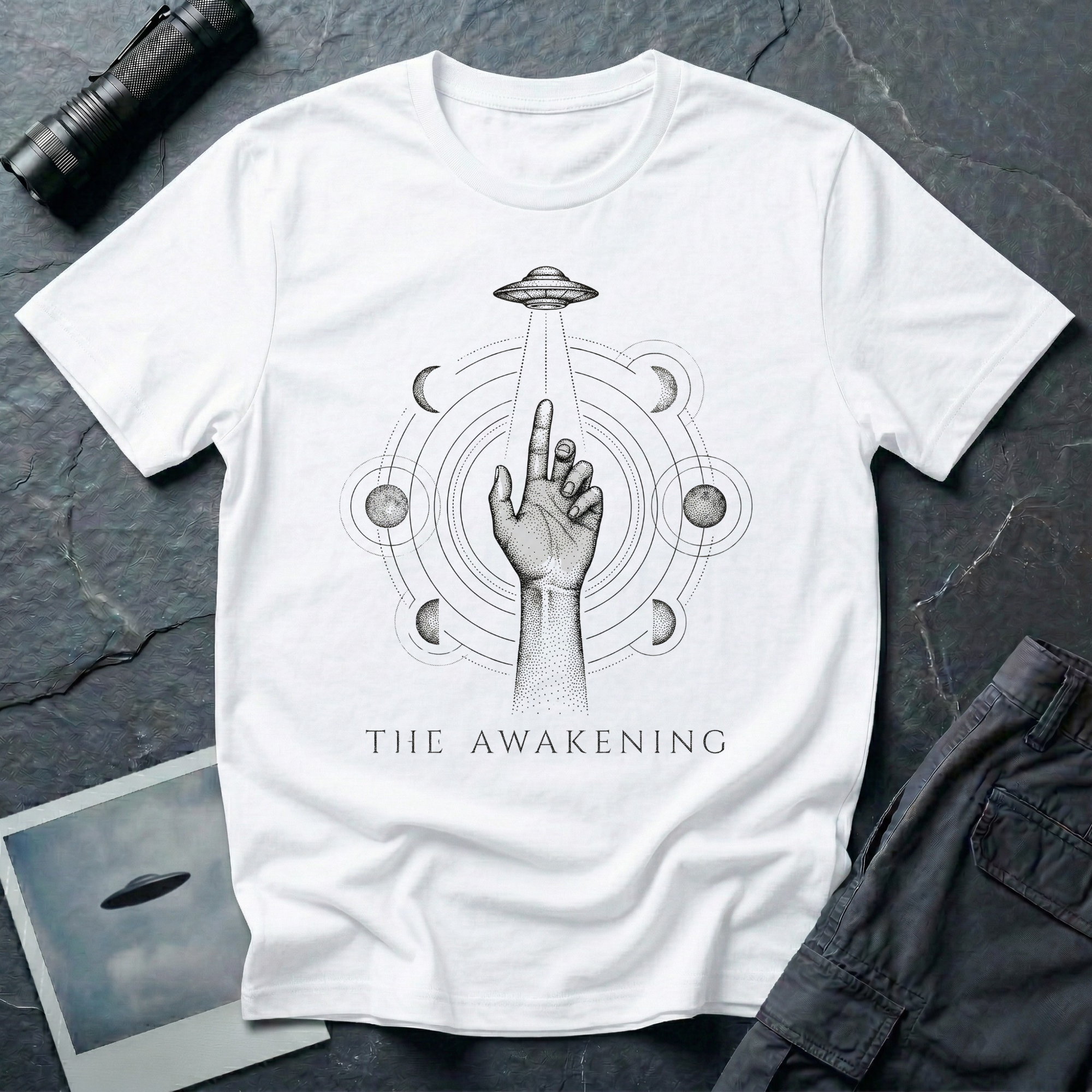The Awakening mystical UFO t-shirt — hand reaching toward flying saucer beam surrounded by six moon phases in stippled black dotwork on white cotton tee
