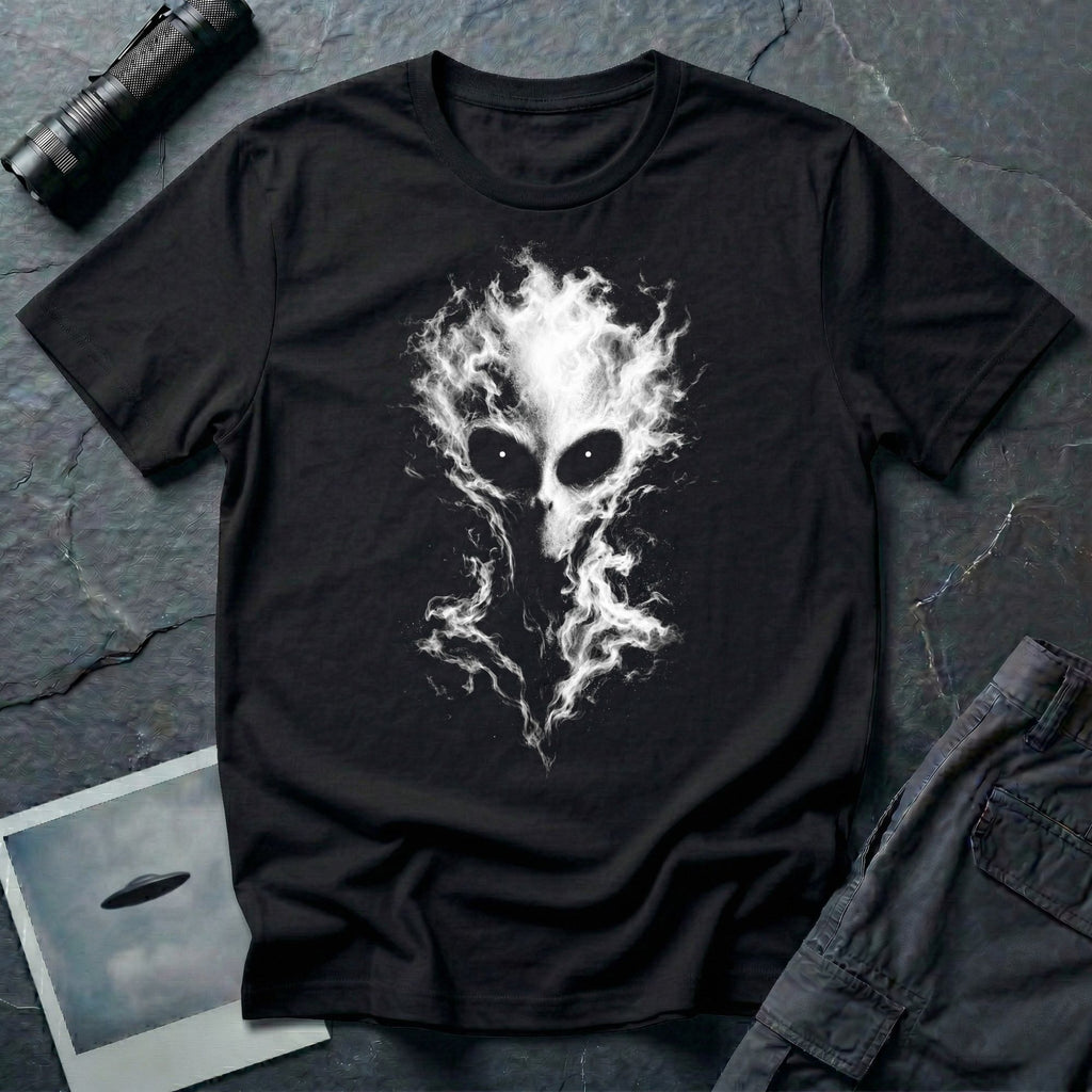 Alien t-shirt laid flat on a dark textured surface, featuring a large white and gray alien head made of smoke, with glowing eyes, black
