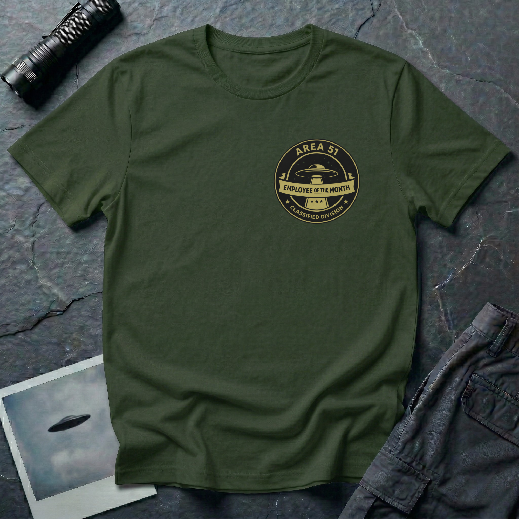 Area 51 Employee Of The Month UFO t-shirt — vintage circular badge with classic flying saucer, "Area 51" and "Classified Division" arc text, "Employee of the Month" ribbon banner in olive and black on upper-left chest of green cotton tee
