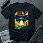 Black t-shirt with vintage flat-graphic illustration of a saucer beaming light over a Nevada desert highway with AREA 51 TOURIST text in gold and white