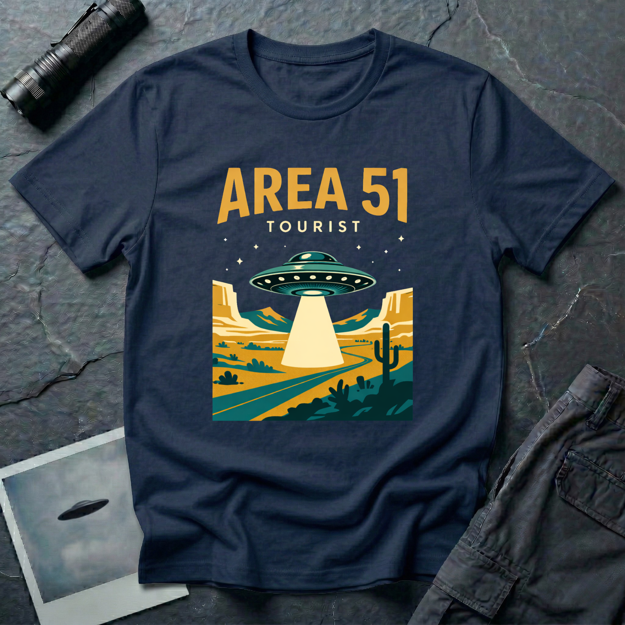 Navy blue t-shirt with vintage flat-graphic illustration of a saucer beaming light over a Nevada desert highway with AREA 51 TOURIST text in gold and white