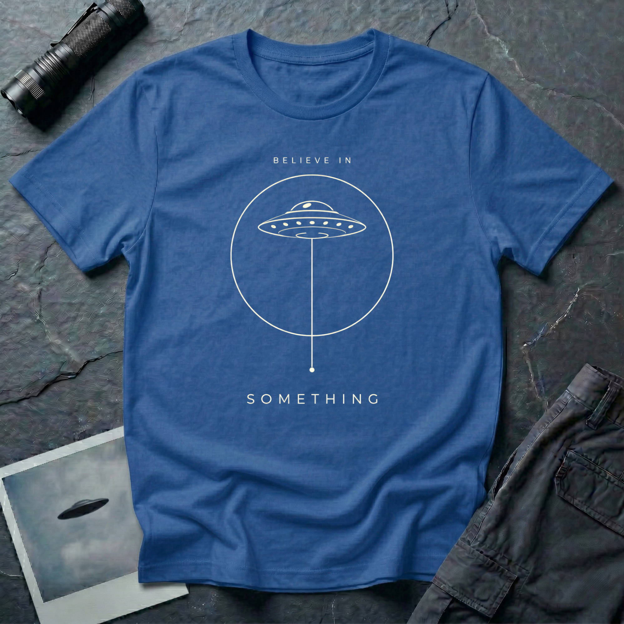 Believe in Something minimalist UFO t-shirt — flying saucer inside a circle with a suspended plumb line in cream on blue cotton tee