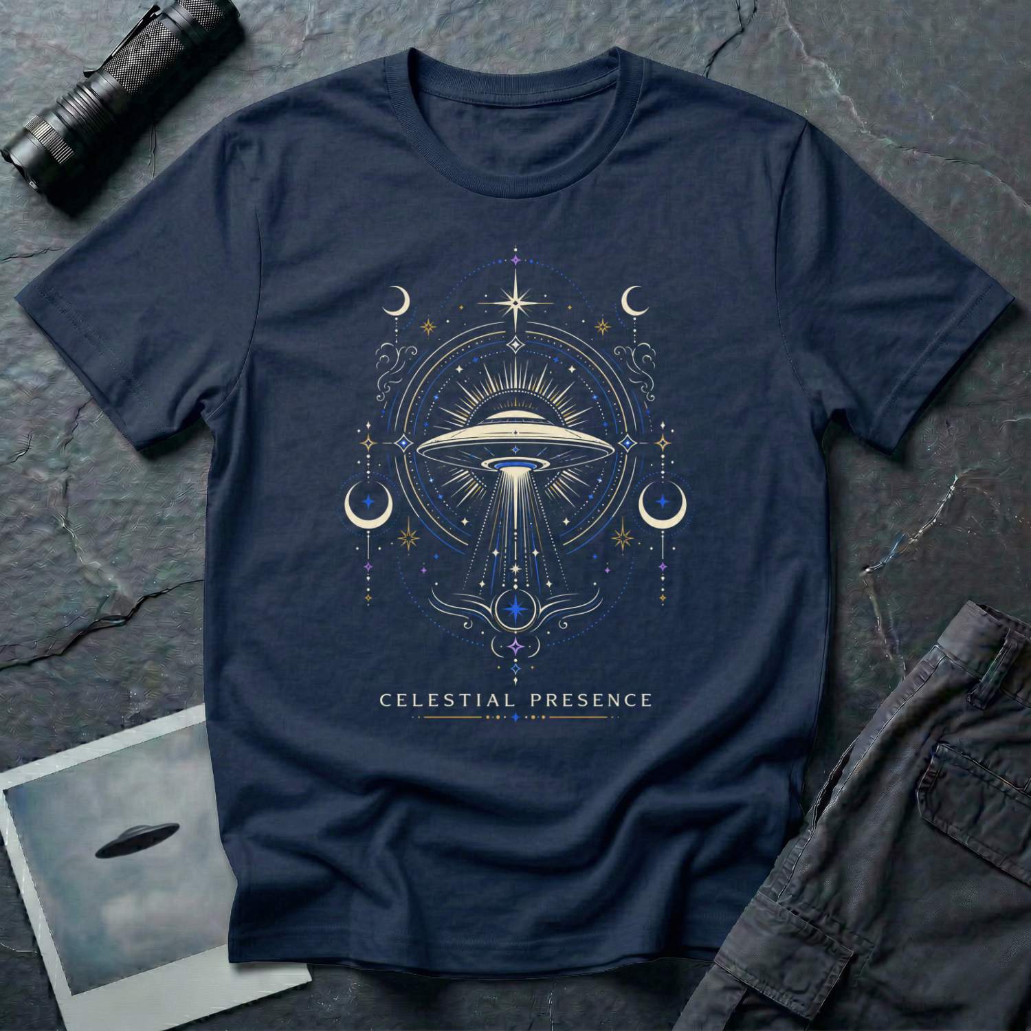 Navy blue t-shirt with a symmetrical celestial UFO illustration featuring crescent moons, four-pointed stars and ornate scrollwork framing a central saucer in gold and blue linework with CELESTIAL PRESENCE caption