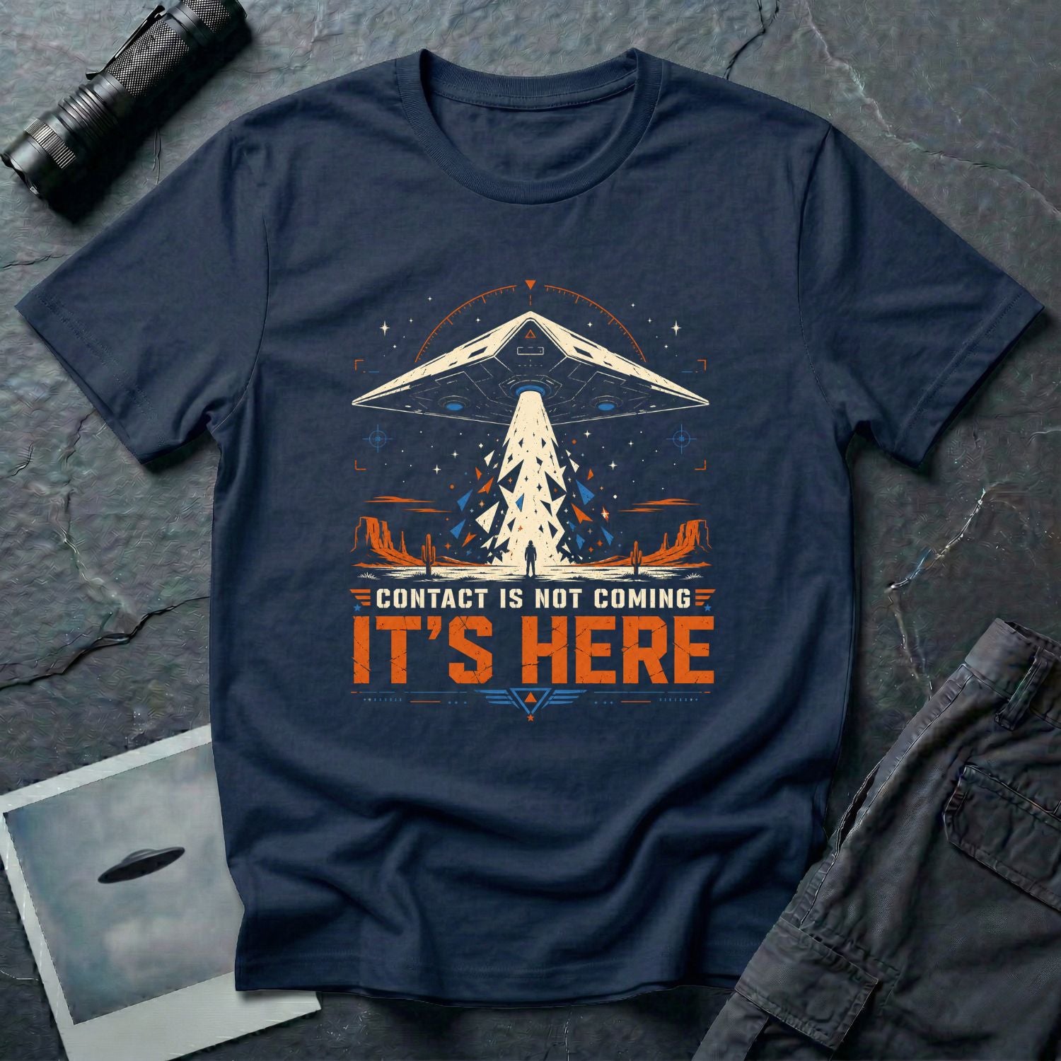 Navy blue t-shirt with cinematic triangular TR-3B UAP craft firing geometric beam shards onto lone human figure in desert landscape with CONTACT IS NOT COMING IT'S HERE text in white and orange