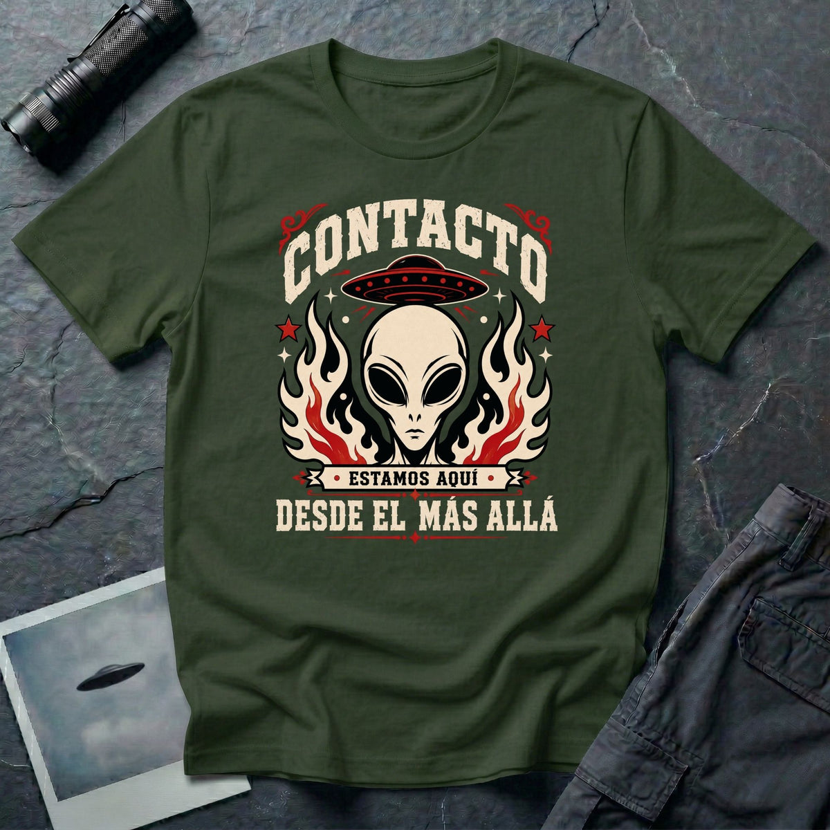 Green t-shirt with vintage rock poster style alien head, UFO, and Spanish text reading Contacto Estamos Aquí Desde El Más Allá