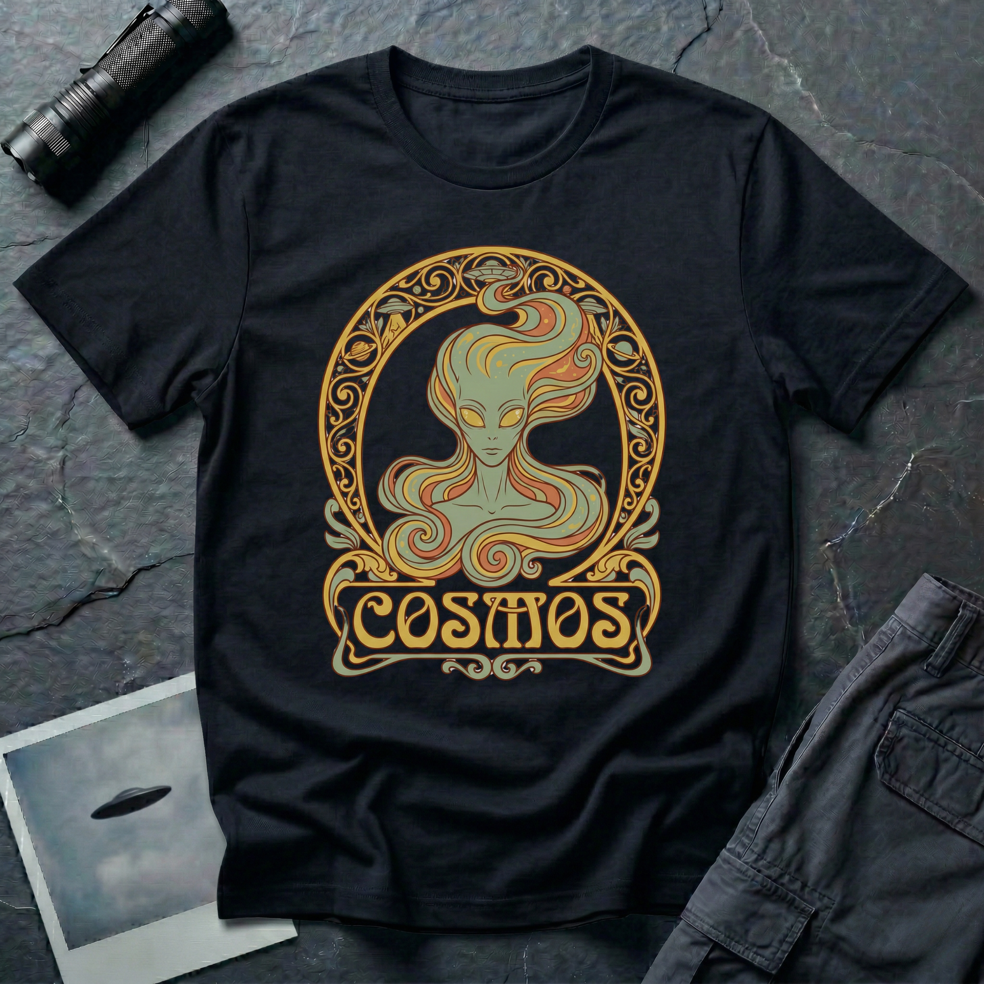 Cosmos Art Nouveau alien t-shirt — green grey alien portrait with large almond eyes and flowing orange hair in ornate gold decorative frame with scrollwork and "Cosmos" banner on black cotton tee