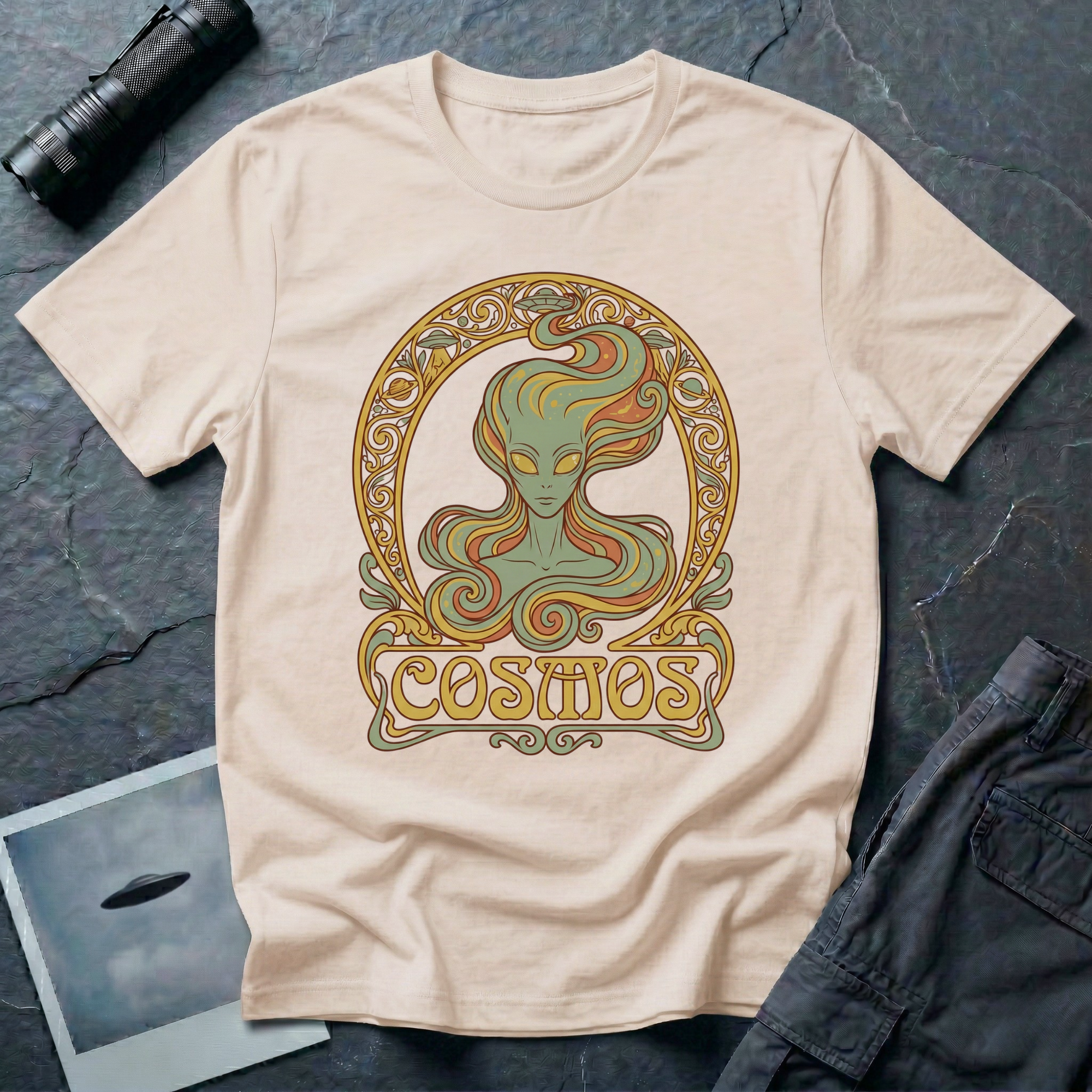 Cosmos Art Nouveau alien t-shirt — green grey alien portrait with large almond eyes and flowing orange hair in ornate gold decorative frame with scrollwork and "Cosmos" banner on natural cotton tee