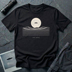Desert Crossing UFO T-shirt with a black flying saucer crossing a white moon above minimalist line-art desert dunes, black tee