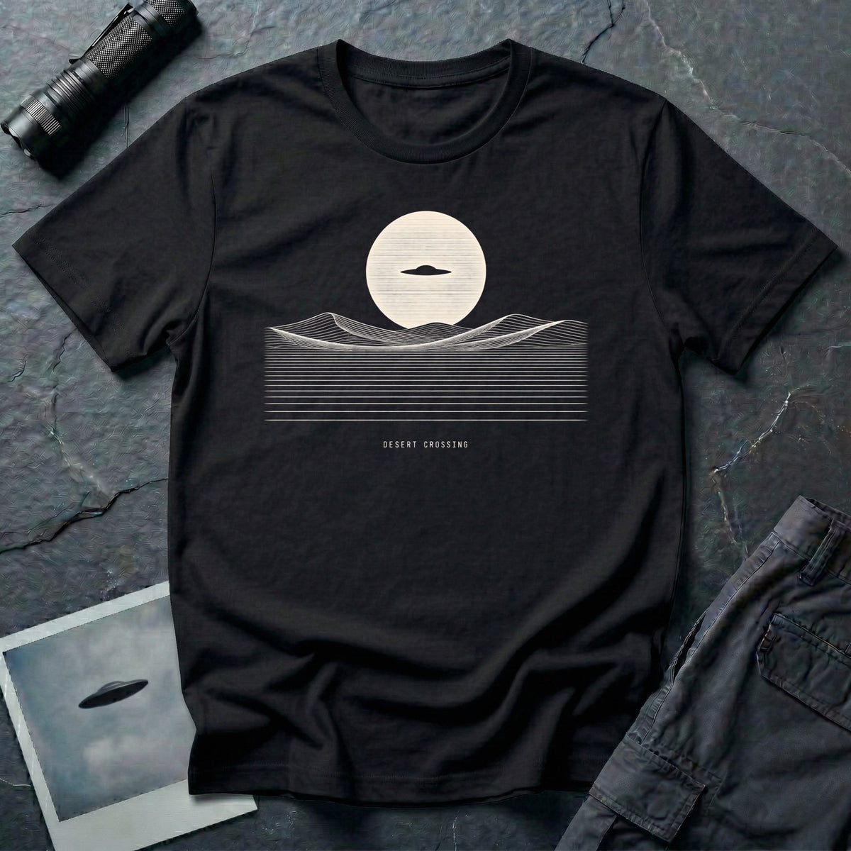Desert Crossing UFO T-shirt with a black flying saucer crossing a white moon above minimalist line-art desert dunes, black tee