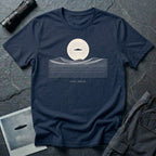 Desert Crossing UFO T-shirt with a black flying saucer crossing a white moon above minimalist line-art desert dunes, navy blue tee