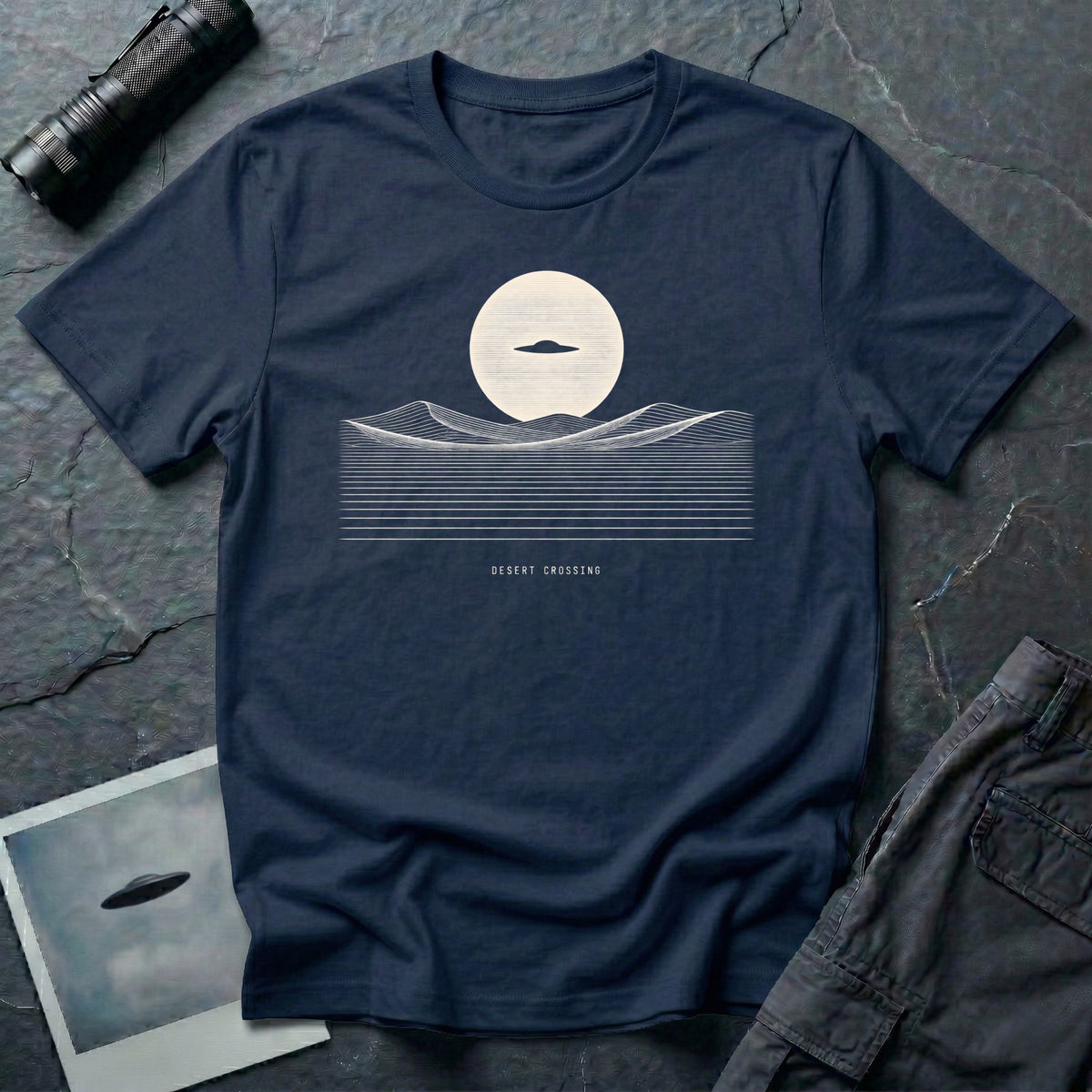 Desert Crossing UFO T-shirt with a black flying saucer crossing a white moon above minimalist line-art desert dunes, navy blue tee
