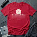 Desert Crossing UFO T-shirt with a black flying saucer crossing a white moon above minimalist line-art desert dunes, red tee