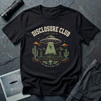 Black t-shirt with vintage collegiate Disclosure Club badge featuring Area 51 facility saucer abduction scene EST 1947 and alien face emblem in cream olive and orange