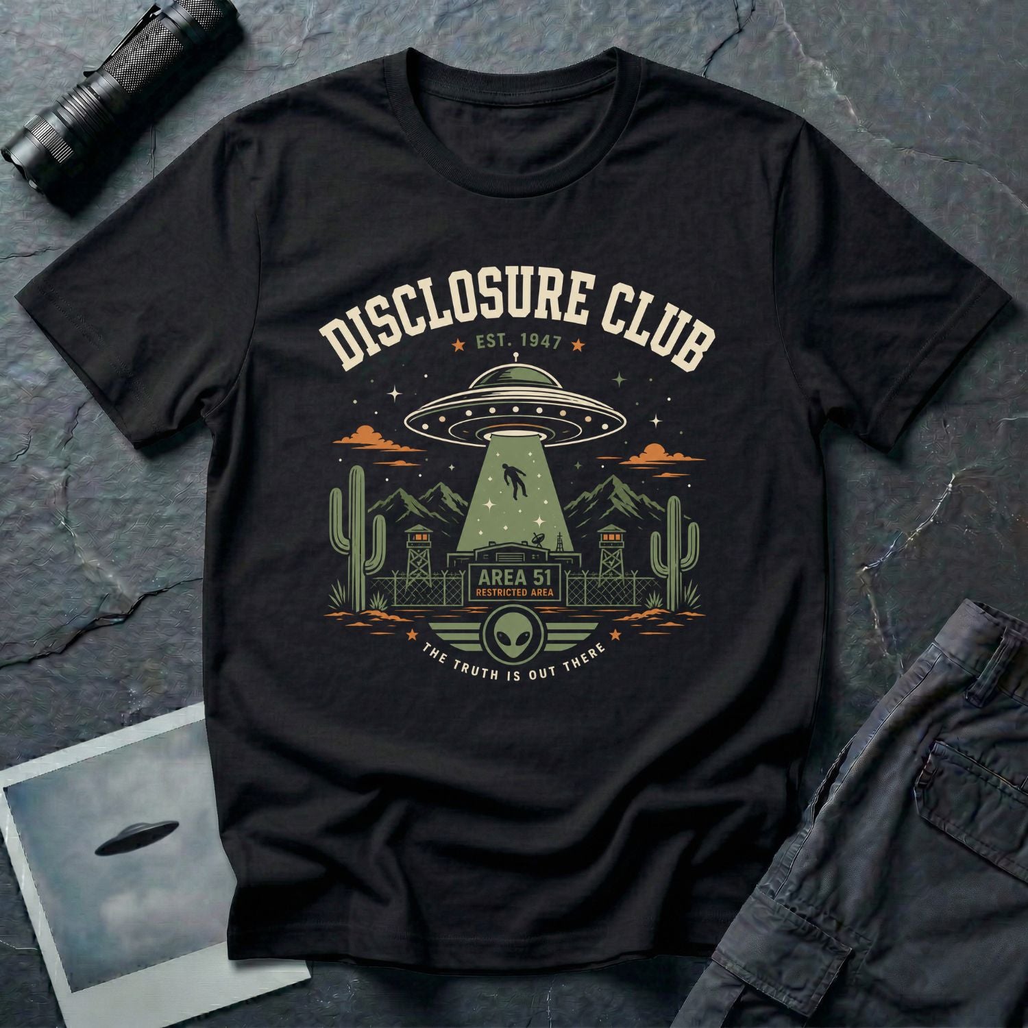 Black t-shirt with vintage collegiate Disclosure Club badge featuring Area 51 facility saucer abduction scene EST 1947 and alien face emblem in cream olive and orange