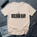 Natural UFO disclosure t-shirt with bold block letters reading DISCLOSURE READY and subtitle CONTACT EXPECTED with a small flying saucer above the horizon in black