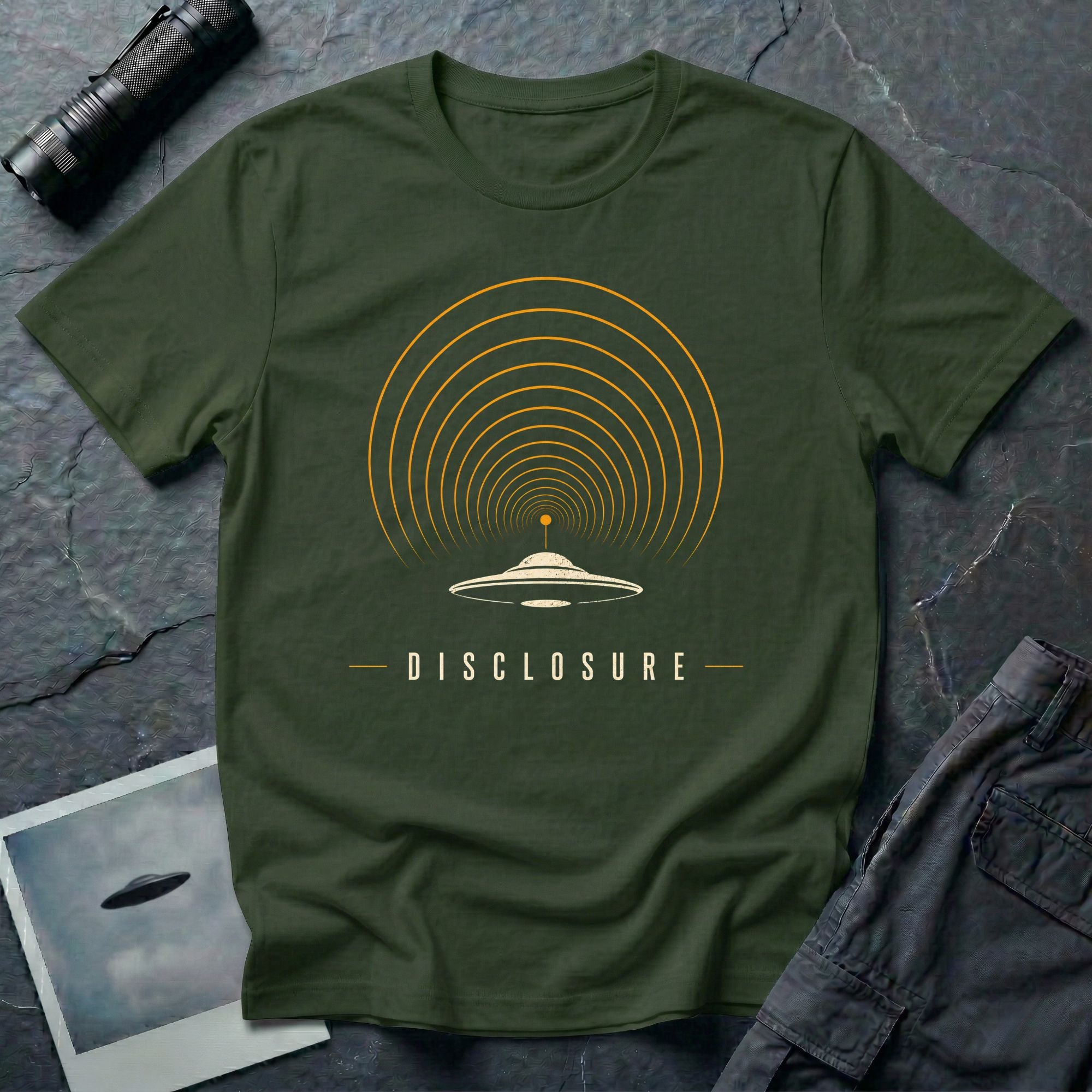 Green UFO disclosure t-shirt with a flying saucer broadcasting concentric signal arcs upward in orange and cream with the word DISCLOSURE beneath