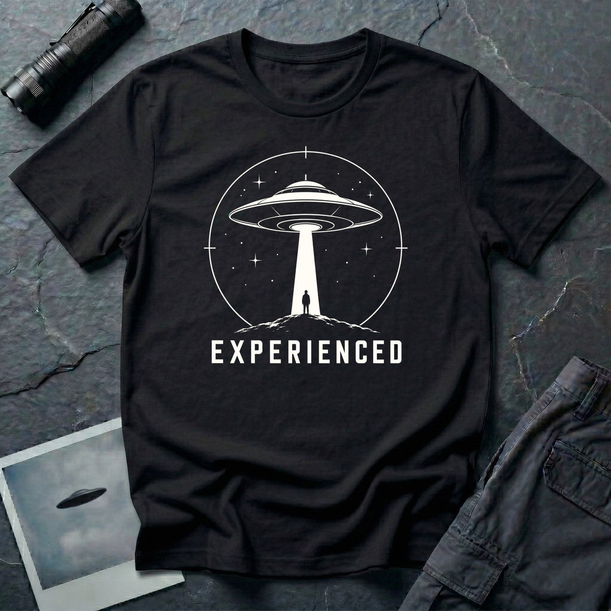 Experienced UFO T-shirt with a lone figure standing beneath the beam of a flying saucer inside a circular night-sky design. Black tee