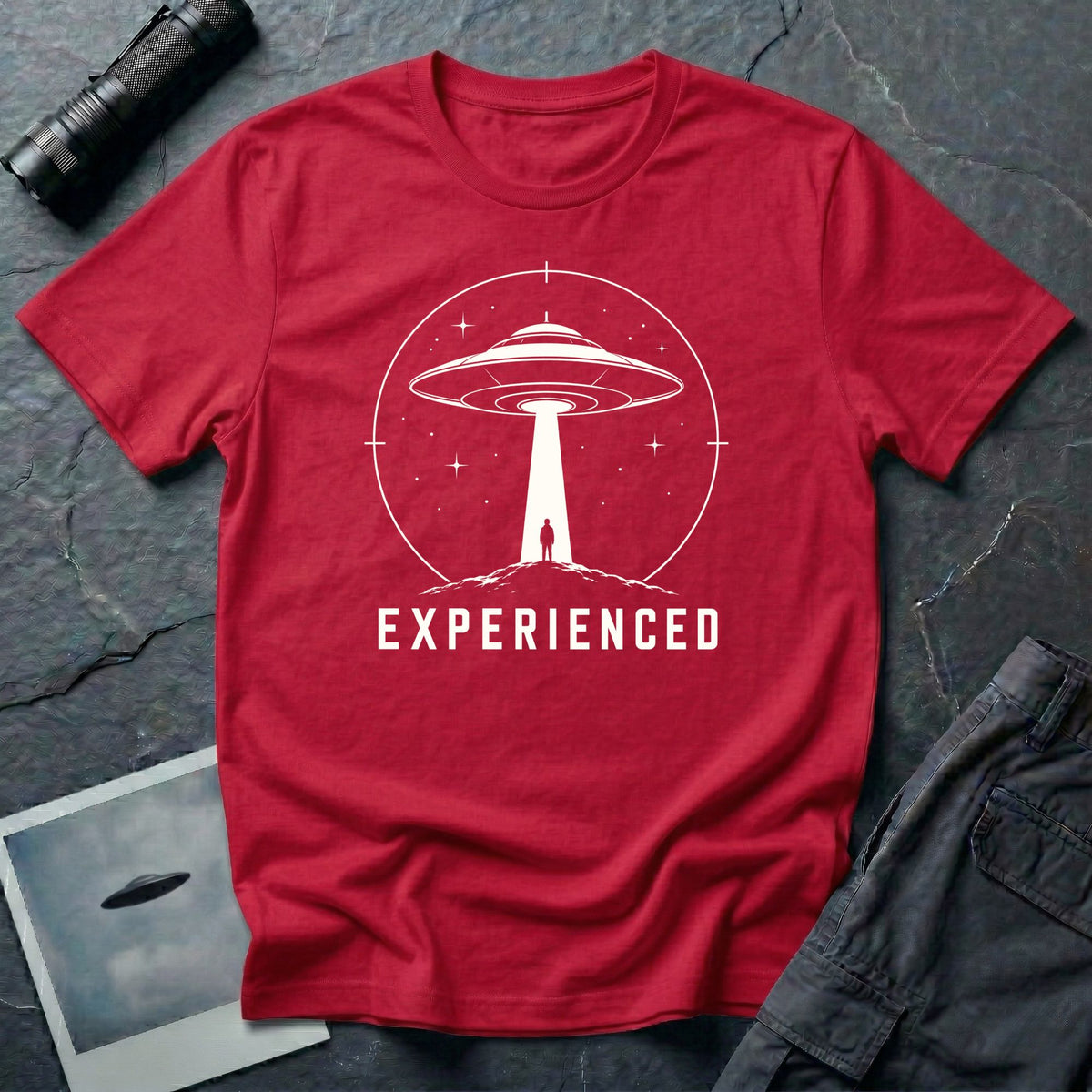 Experienced UFO T-shirt with a lone figure standing beneath the beam of a flying saucer inside a circular night-sky design. Red tee