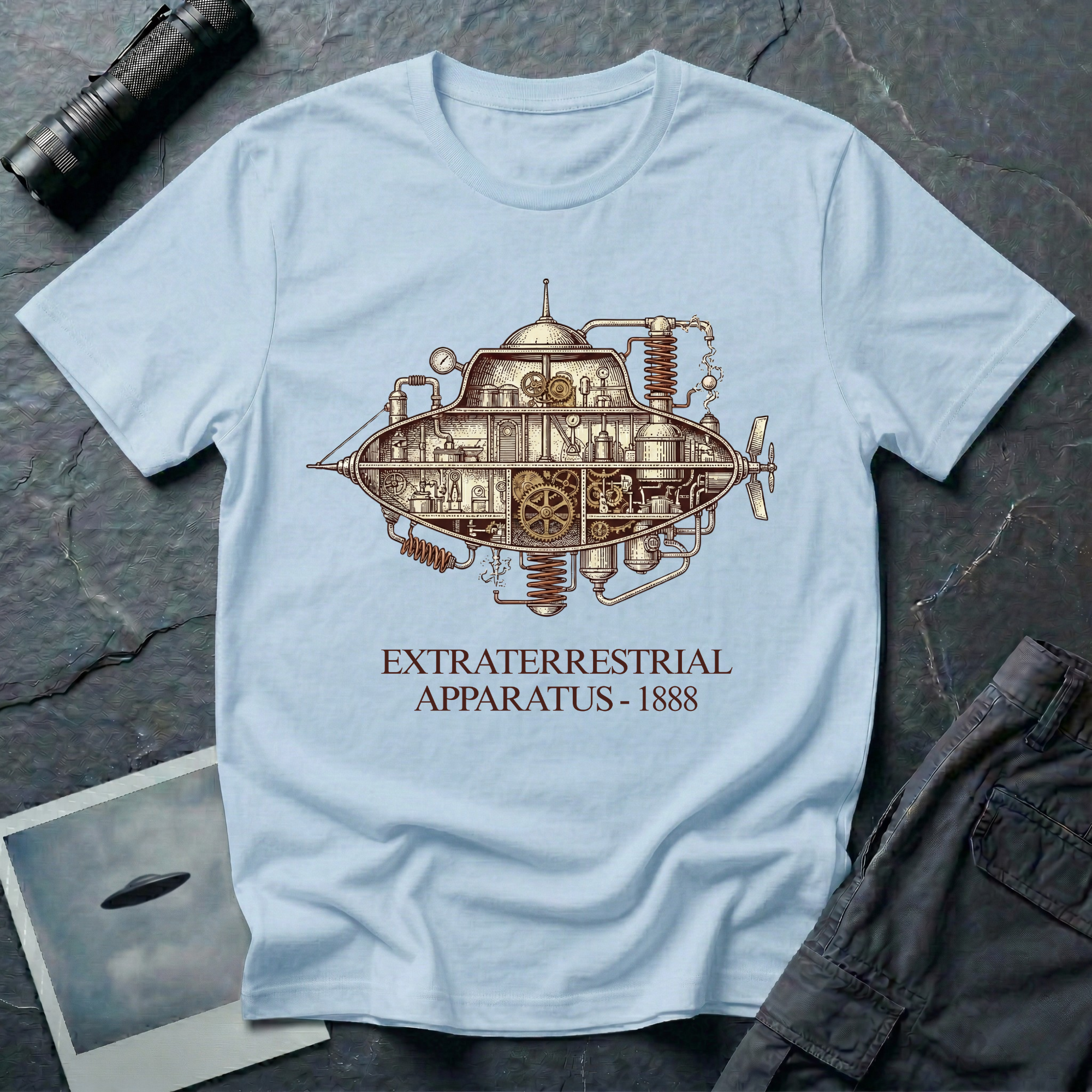 Extraterrestrial Apparatus steampunk UFO t-shirt — Victorian-era airship with exposed brass machinery gears and copper piping with "Extraterrestrial Apparatus 1888" caption on light blue cotton tee