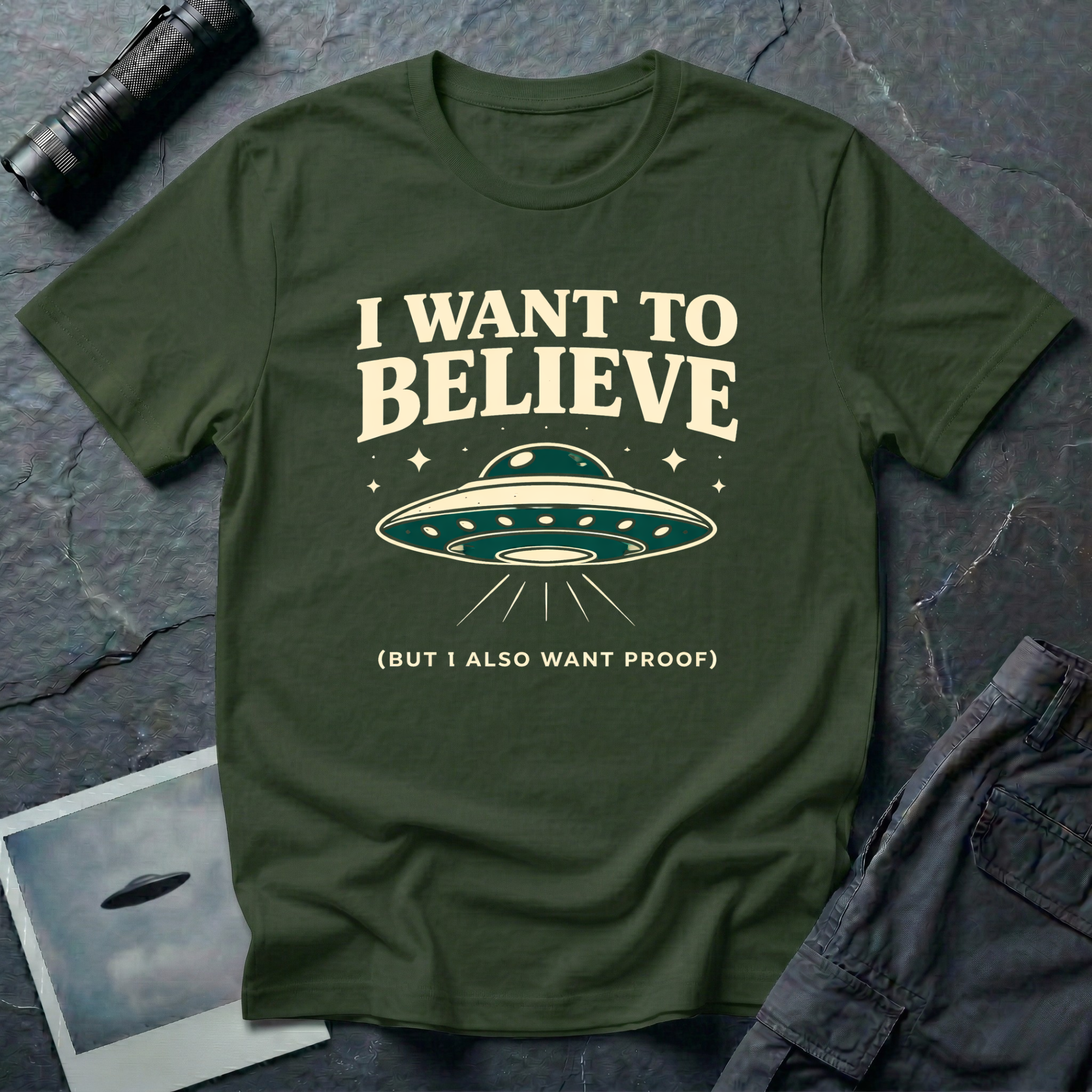 I Want To Believe ironic UFO t-shirt — classic teal saucer with the phrase "I want to believe (but I also want proof)" on military green cotton tee