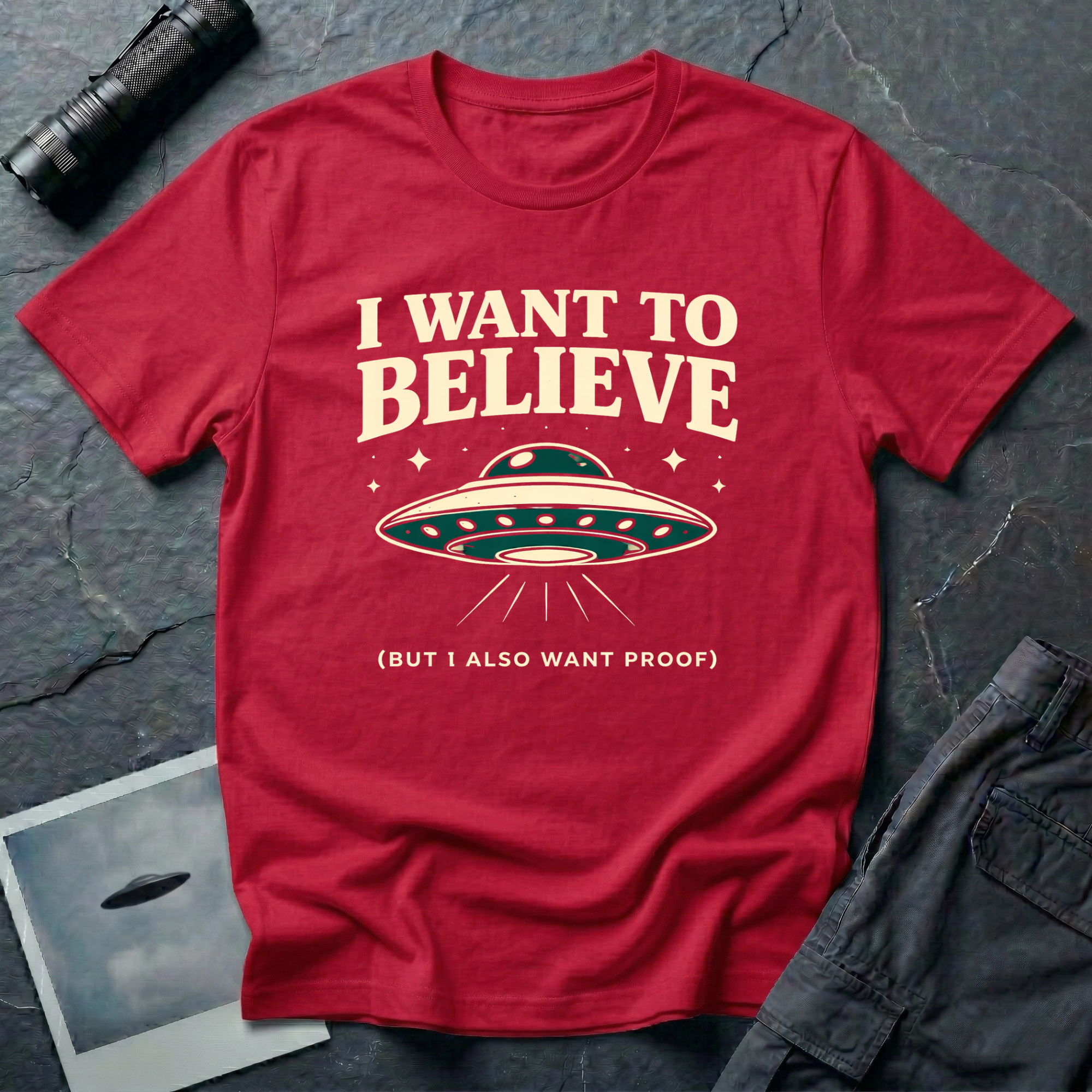 I Want To Believe ironic UFO t-shirt — classic teal saucer with the phrase "I want to believe (but I also want proof)" on red cotton tee