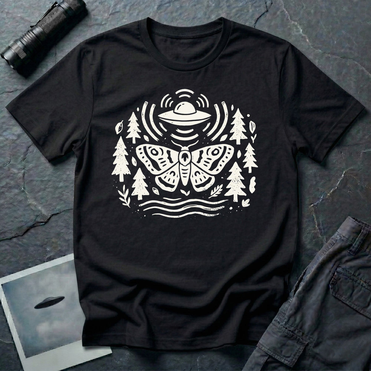 Moth and UFO T-shirt with a folk-art moth beneath a flying saucer, surrounded by pine trees, leaves and radiating signal lines, on black t-shirt