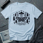 Moth and UFO T-shirt with a folk-art moth beneath a flying saucer, surrounded by pine trees, leaves and radiating signal lines, on light blue t-shirt
