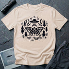 Moth and UFO T-shirt with a folk-art moth beneath a flying saucer, surrounded by pine trees, leaves and radiating signal lines, on natural t-shirt