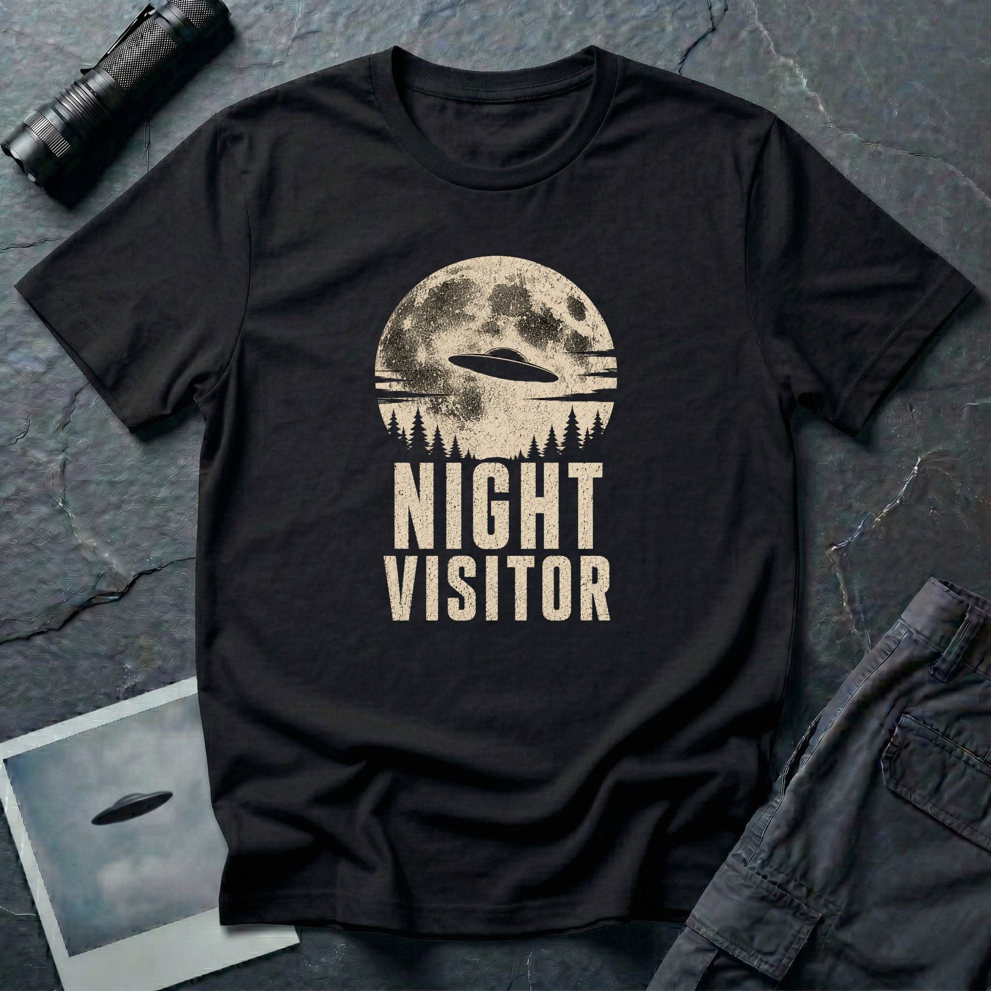 Black retro UFO t-shirt with a flying saucer crossing a full moon over a conifer treeline with the words NIGHT VISITOR in distressed pale lettering