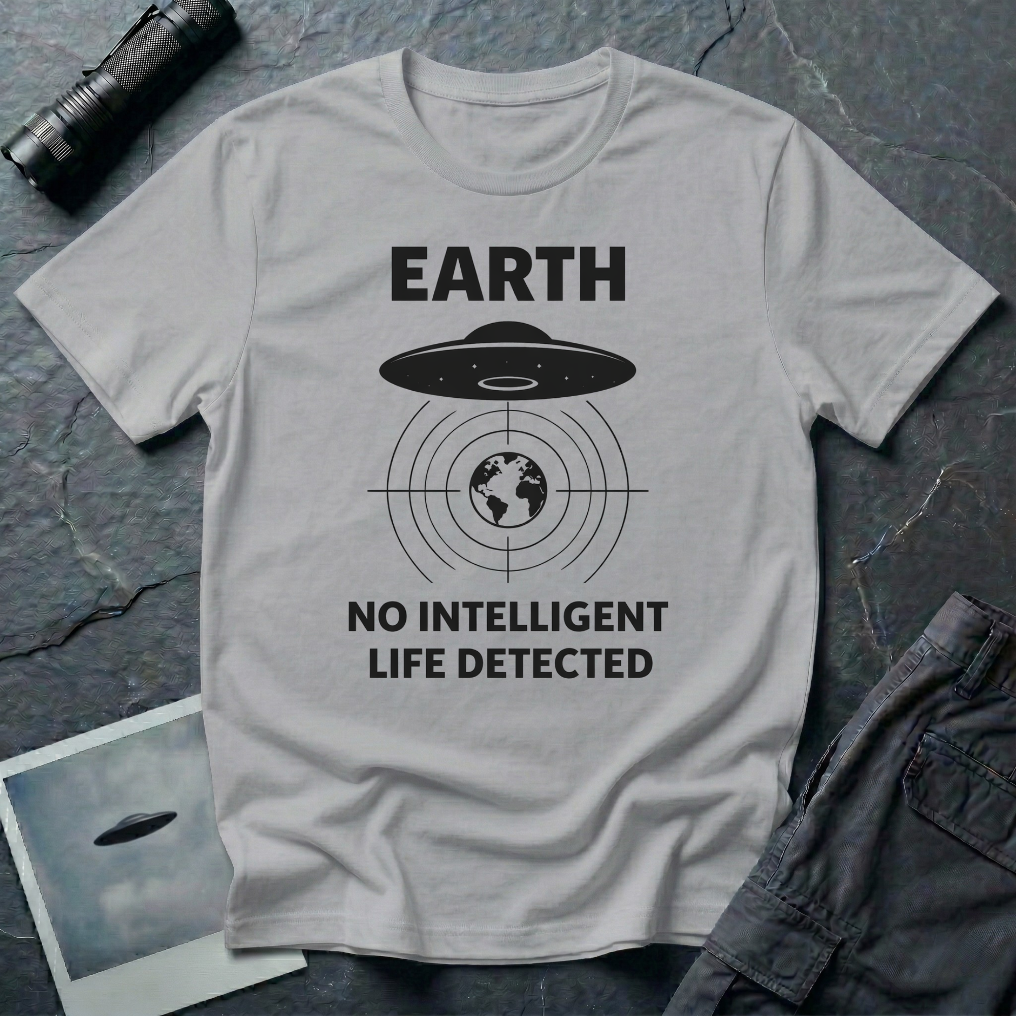 No Intelligent Life Detected UFO t-shirt — classic flying saucer above concentric scan rings and crosshairs targeting Earth with "EARTH / NO INTELLIGENT LIFE DETECTED" caption in black on grey cotton tee