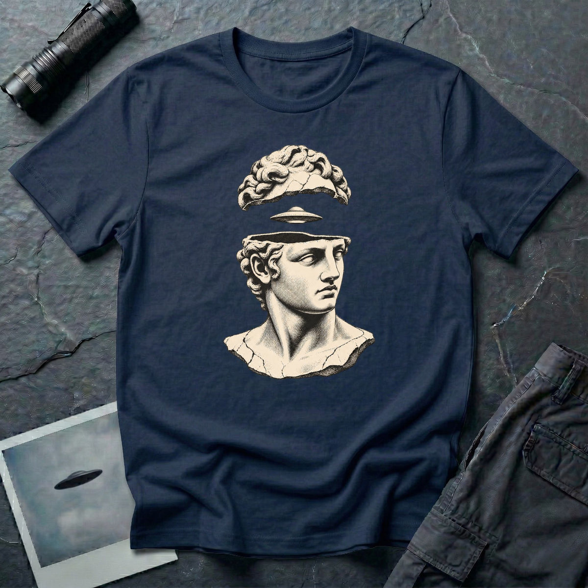 Classical marble bust with the top of the head lifted to reveal a UFO emerging, in cream engraving linework on a navy blu t-shirt