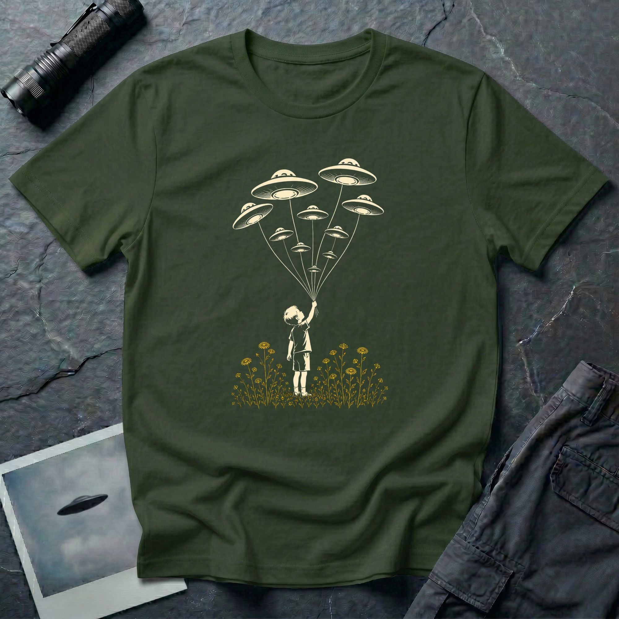 Stencil UFO t-shirt design, child reaching up to hold strings tethered to a small fleet of UFOs, orange wildflowers at the base, green tee