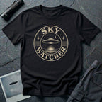 Black retro UFO t-shirt with a distressed circular badge showing a flying saucer over water at night with a crescent moon and the words SKY WATCHER in pale lettering