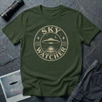 Military green retro UFO t-shirt with a distressed circular badge showing a flying saucer over water at night with a crescent moon and the words SKY WATCHER in pale lettering